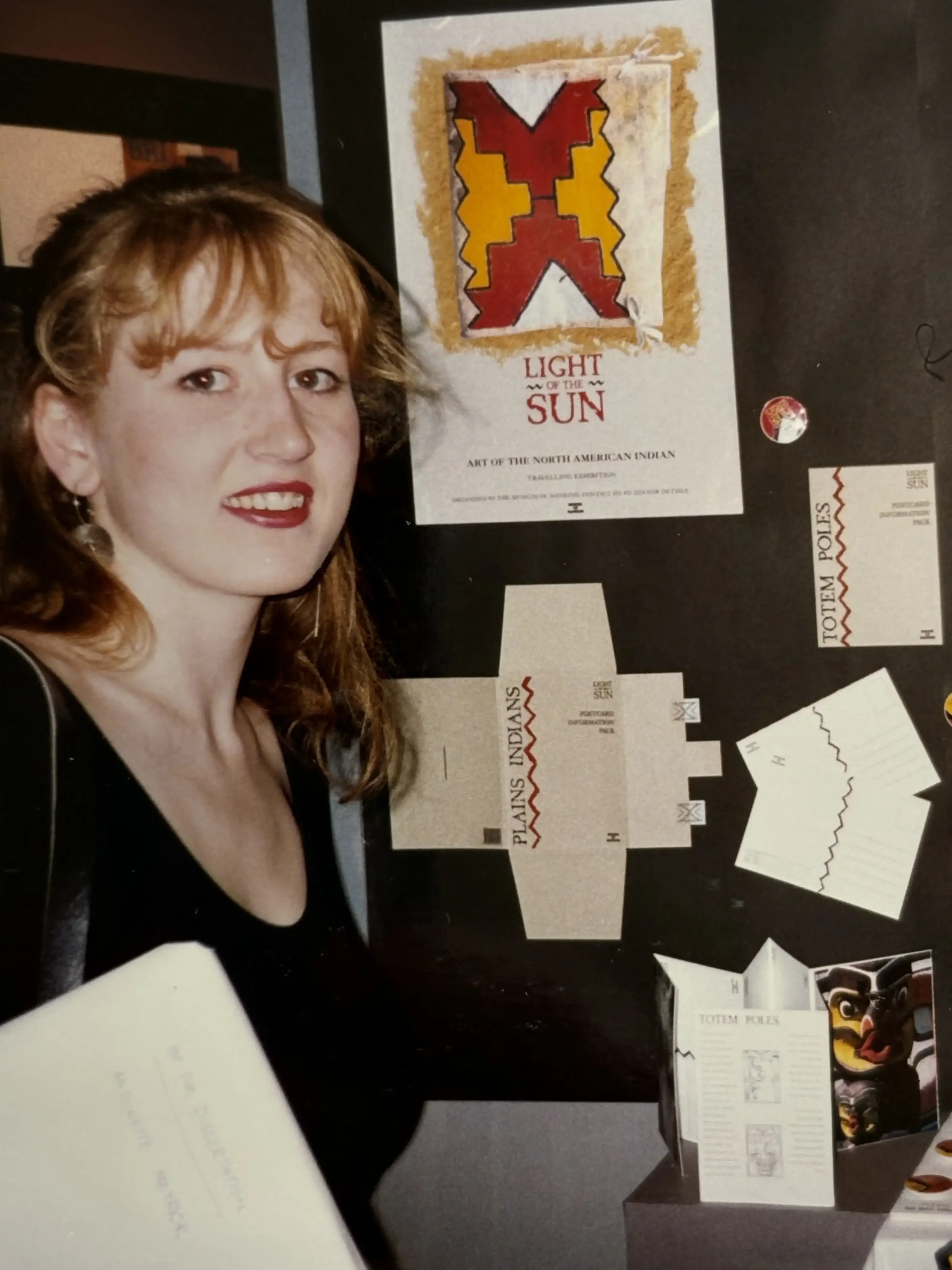 A woman standing next to a display of artwork and paper crafts related to the North American Indian 'Art of the Sun'.