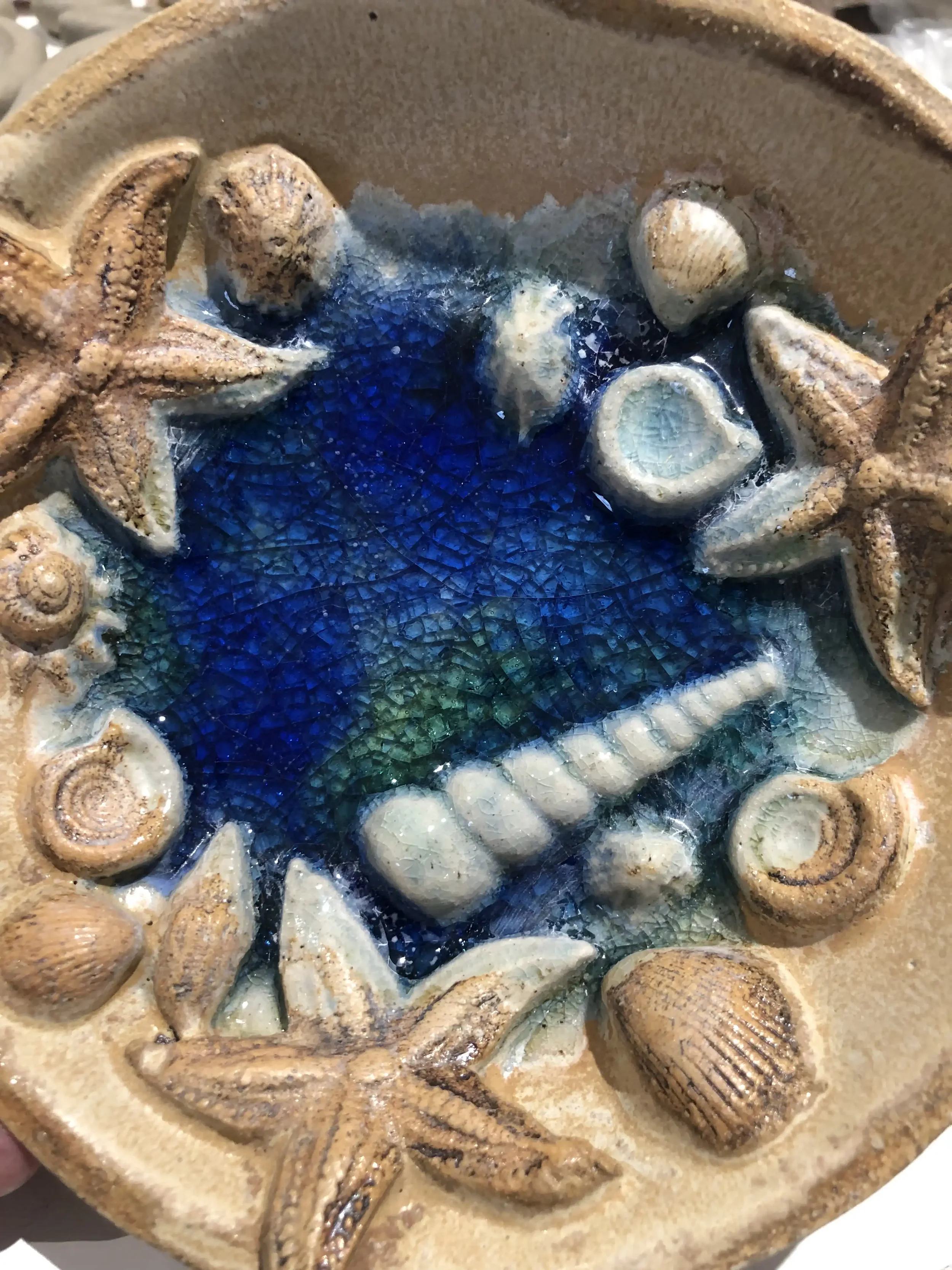 Ceramic bowl with shells and starfish around the border and melted glass in the middle.