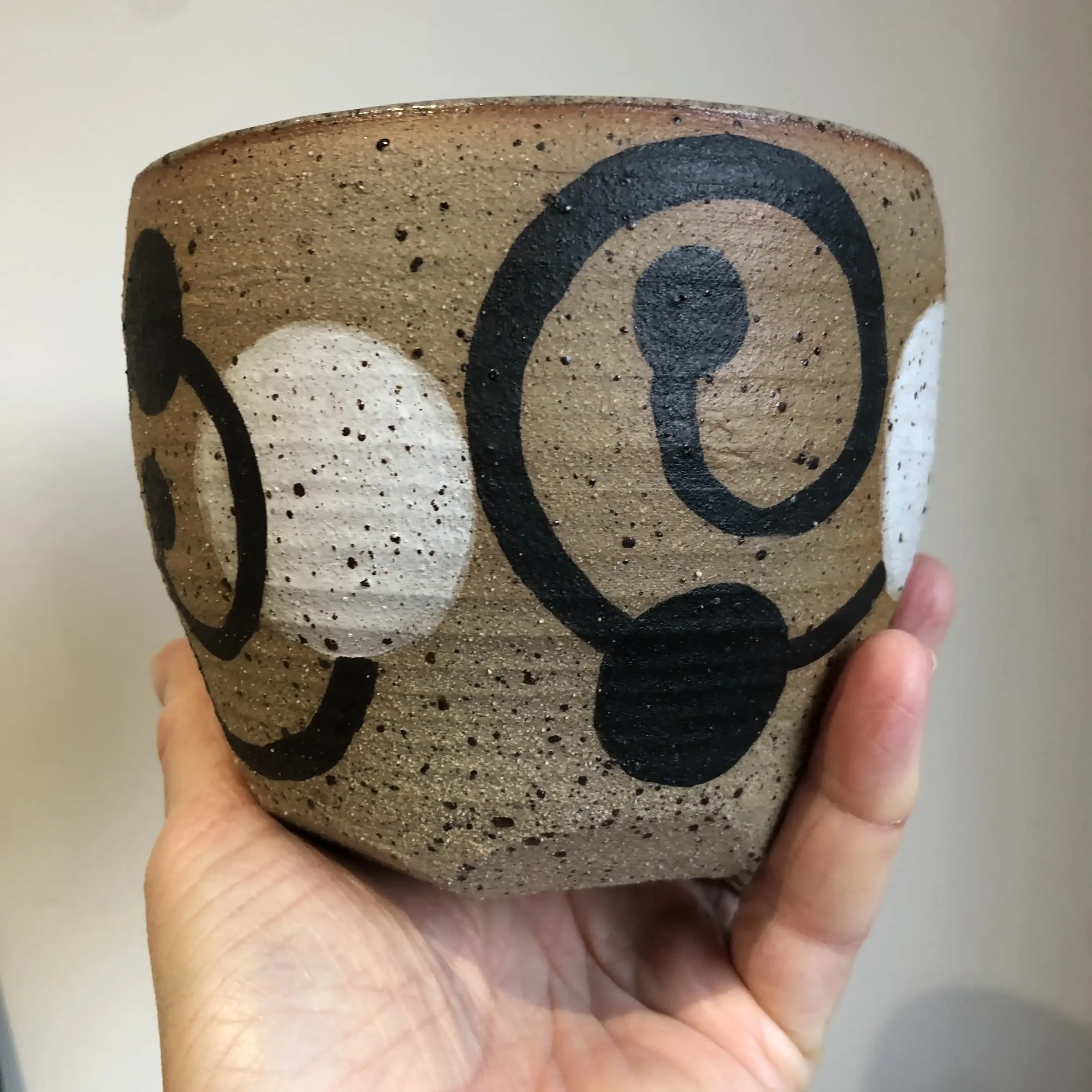 A hand holding a ceramic bowl with a beige background and black and white abstract circular designs.