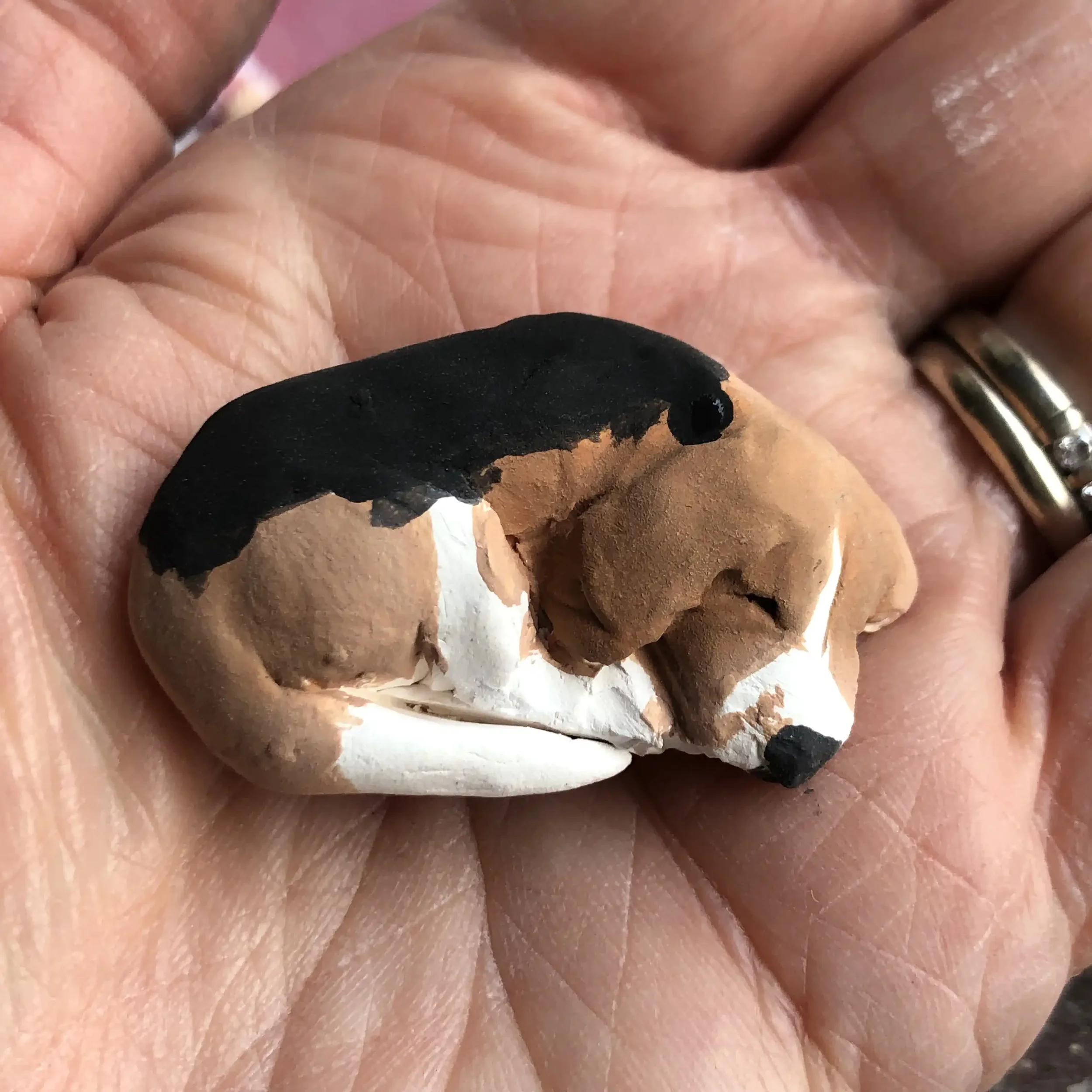 A small porcelain sculpture of a sleeping beagle underglazed with brown, white, and black, held in a person's hand.