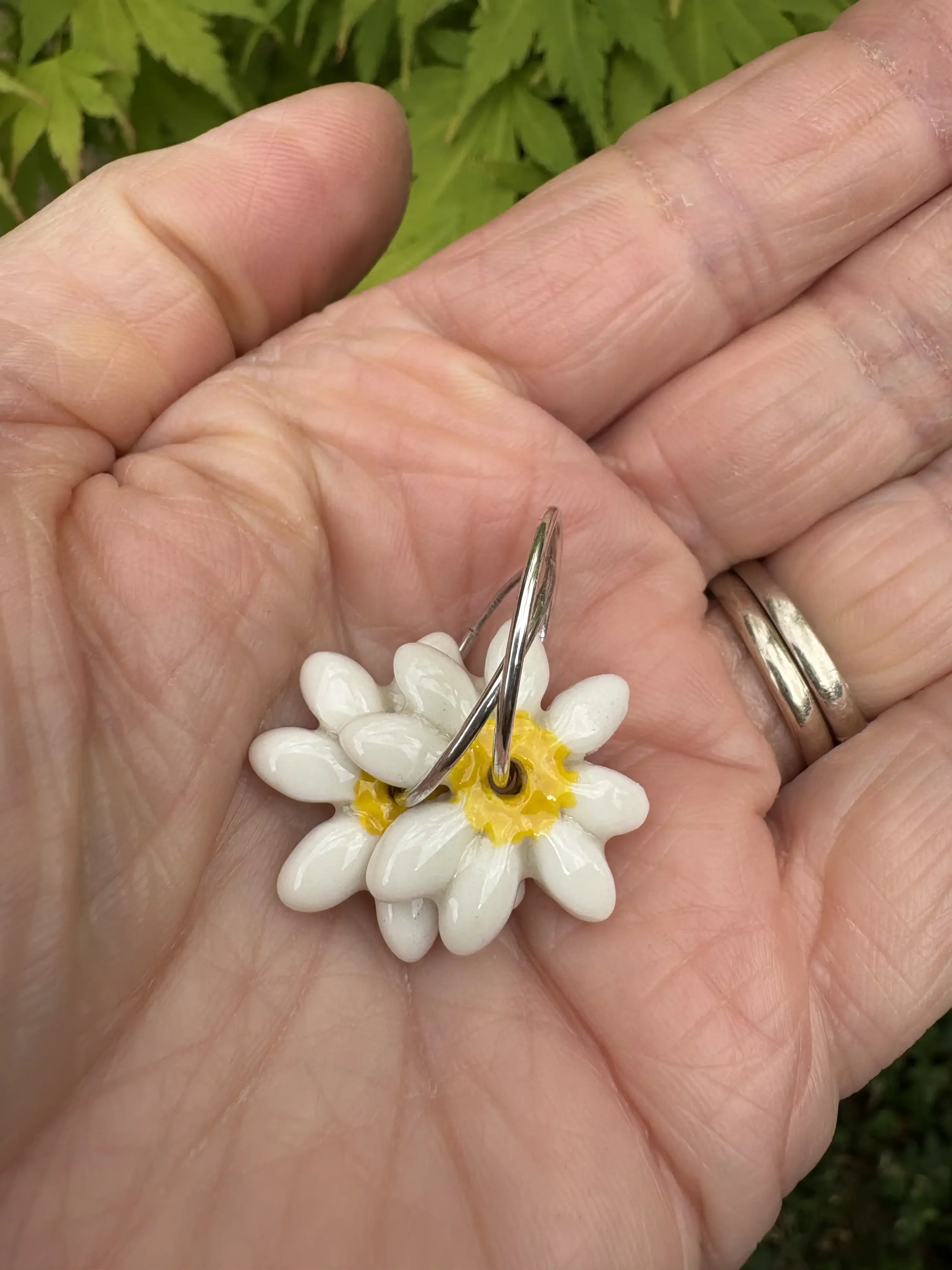 Hand holding a pair of ceramic daisy earrings.