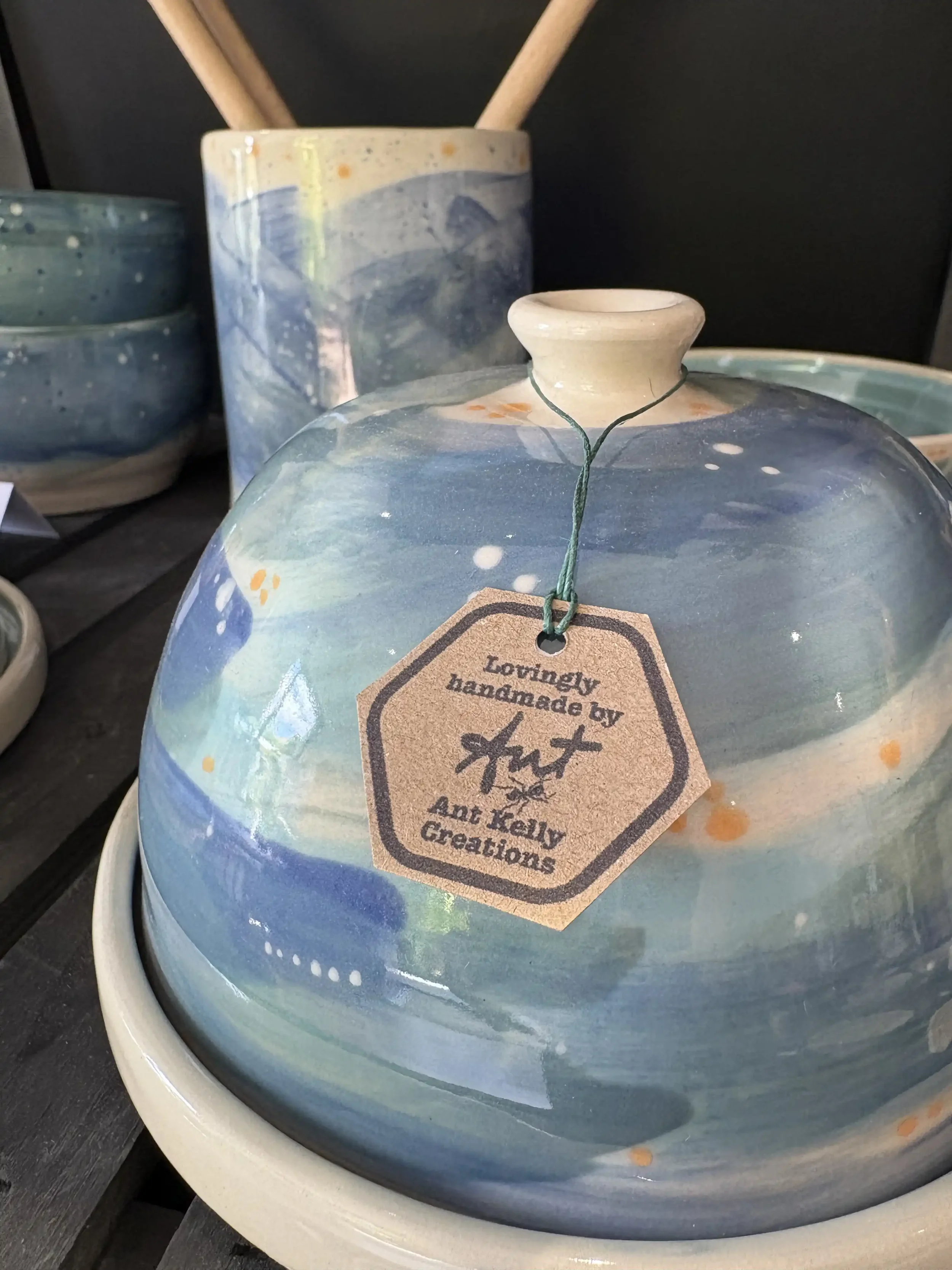Handmade ceramic butter dome and matching plate with a tag reading 'Lovingly handmade by Ant Kelly Creations' on display among other ceramic pieces.