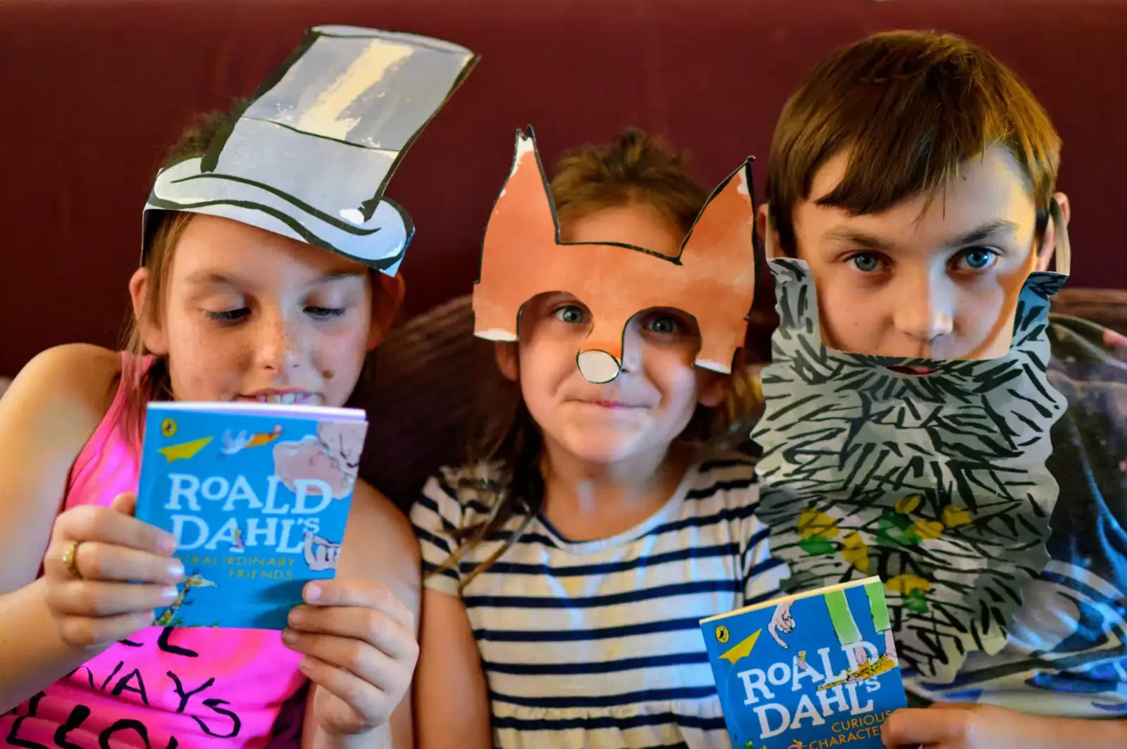 Three children sitting together with McDonald's Happy Meal books, wearing cardboard Roald Dahl's Willy Wonka hat, Fantastic Mr Fox ears and a Mr Twit beard.