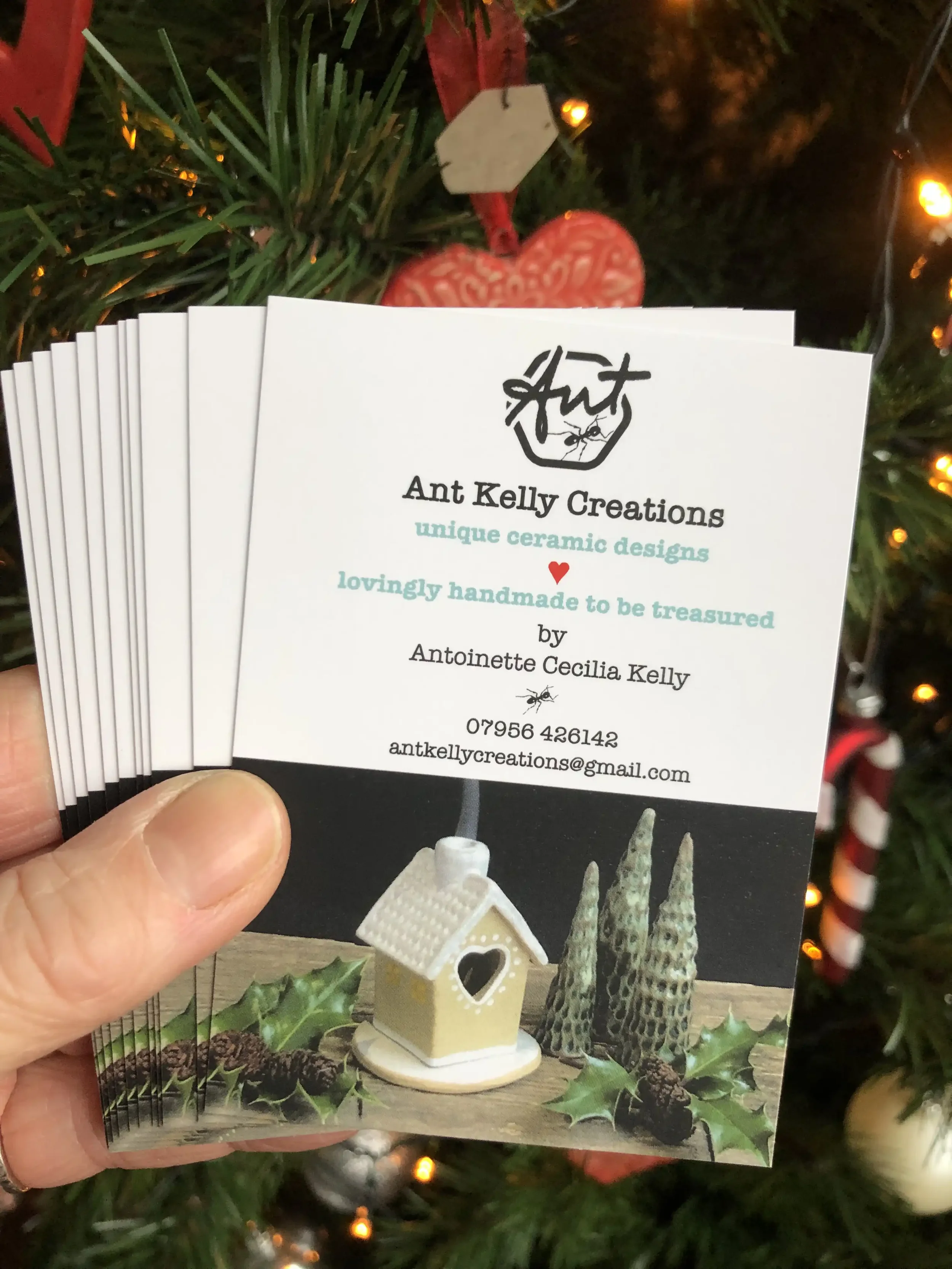 Business cards for Ant Kelly Creations featuring ceramic designs, with a Christmas tree and ornaments in the background.