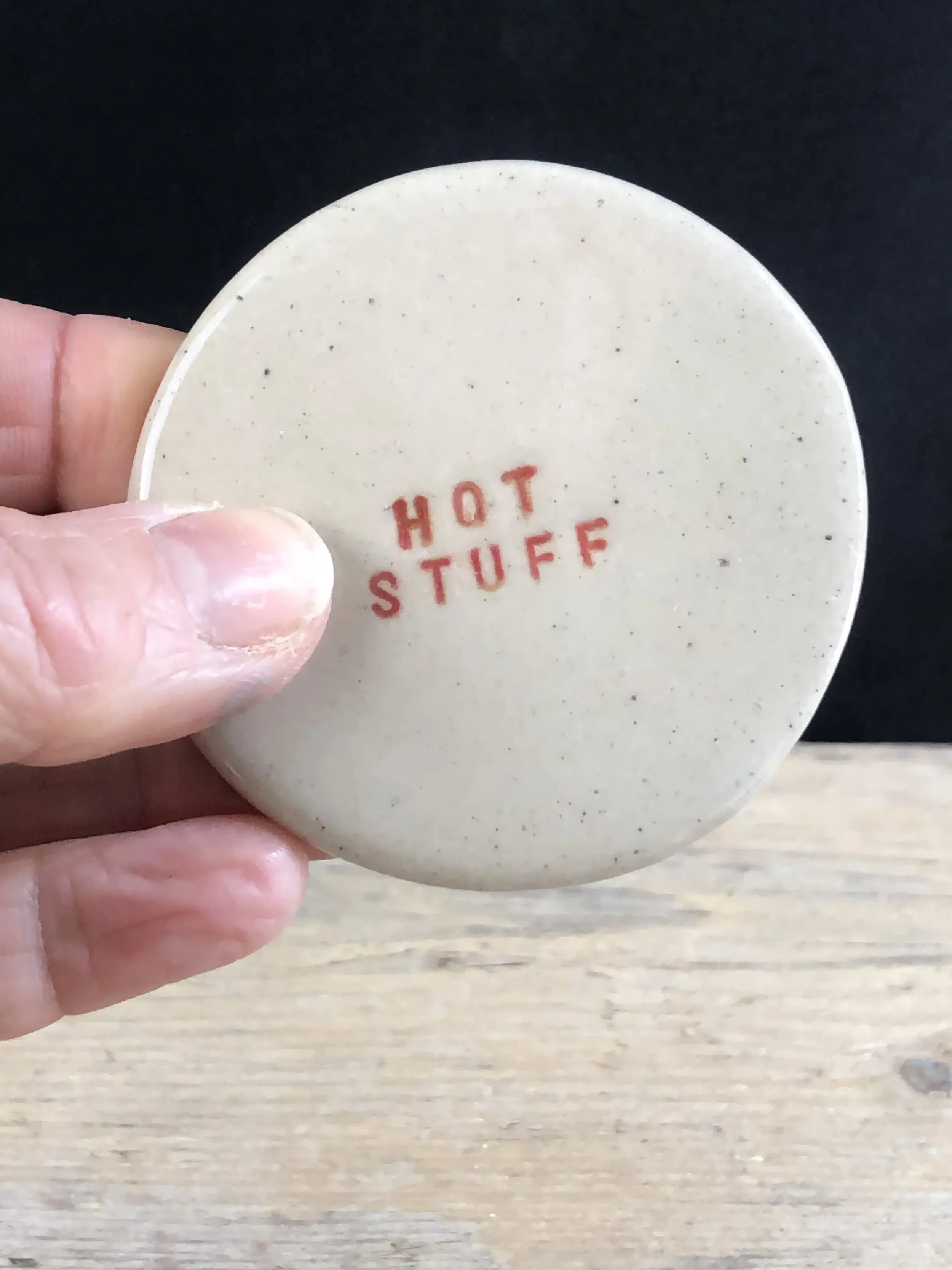 A person's hand holding a circular coaster with the words 'HOT STUFF' stamped in red on the surface.