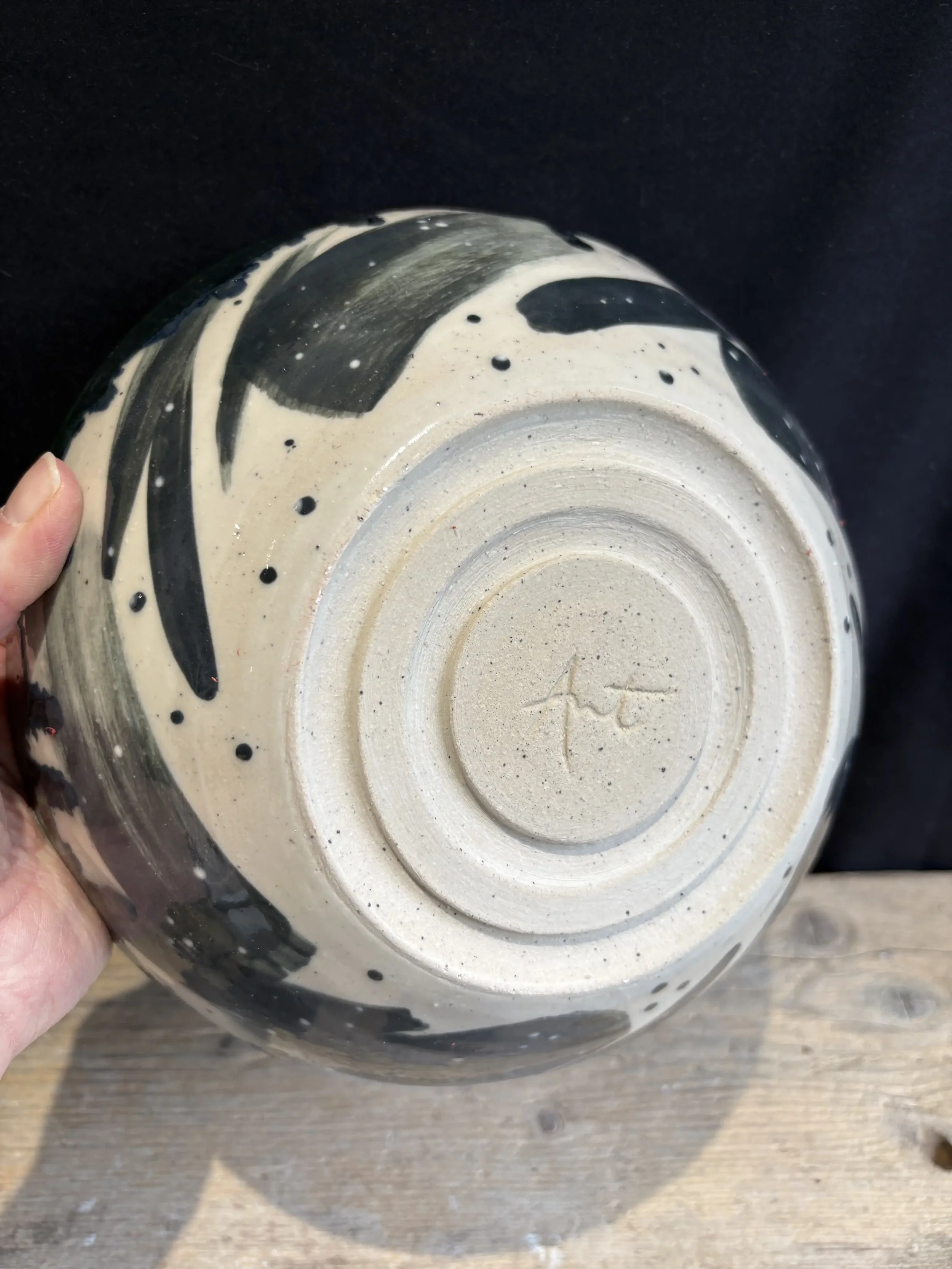 Close-up of the bottom of a ceramic bowl with a black and white splatter glaze design, showing the unglazed ring and signature or maker's mark on the base.