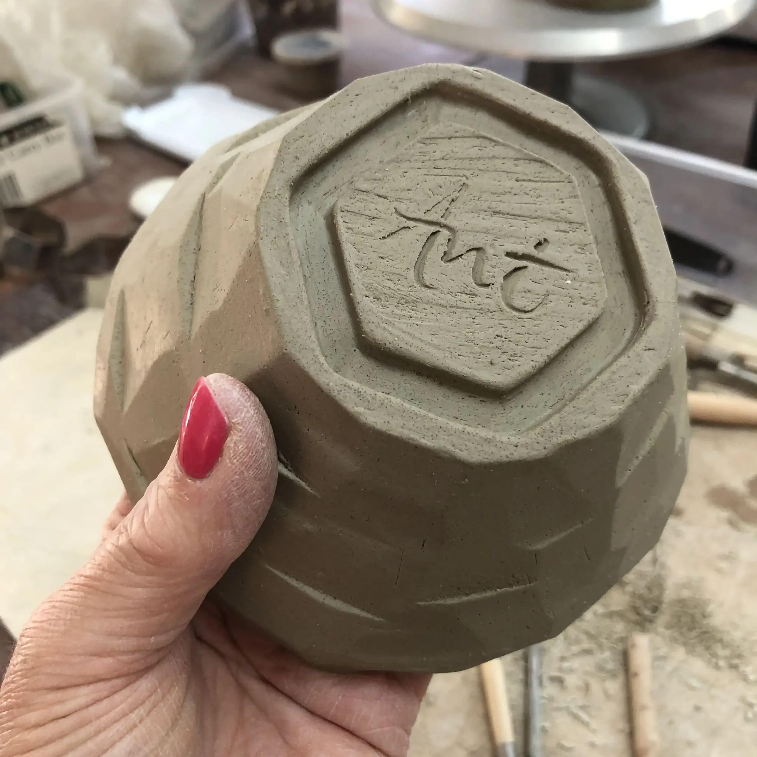 Close-up of a person's hand holding a piece of pottery with 'Ant' carved at the bottom.