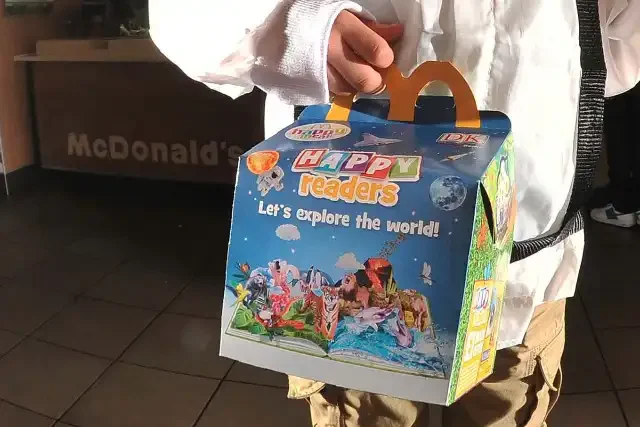 Child holding a McDonald's 'Happy Readers' Happy Meal box with the slogan "Let's explore the world!"