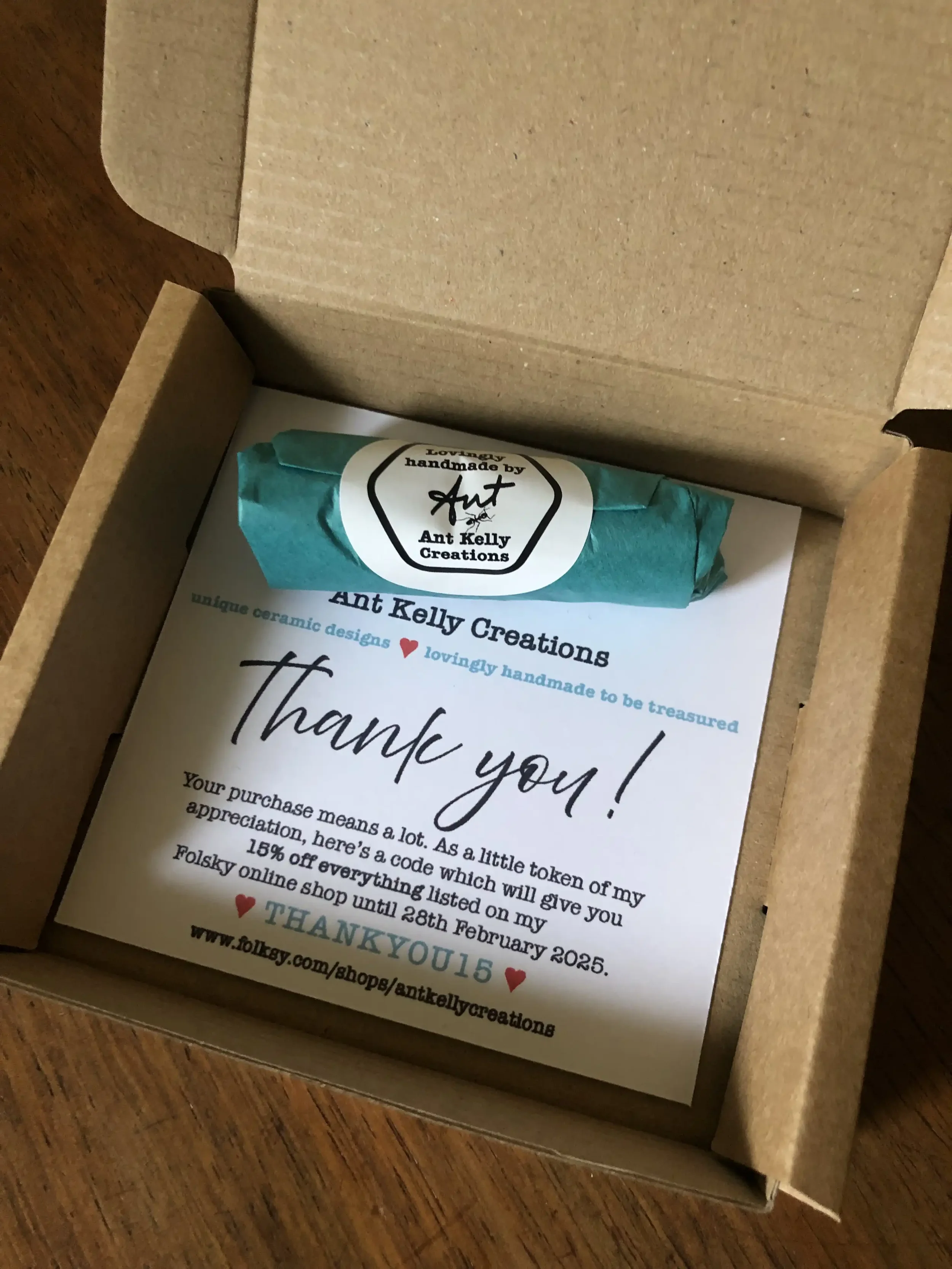 A thank you note from Ant Kelly Creations inside a cardboard box, with a wrapped ceramic item at the top.