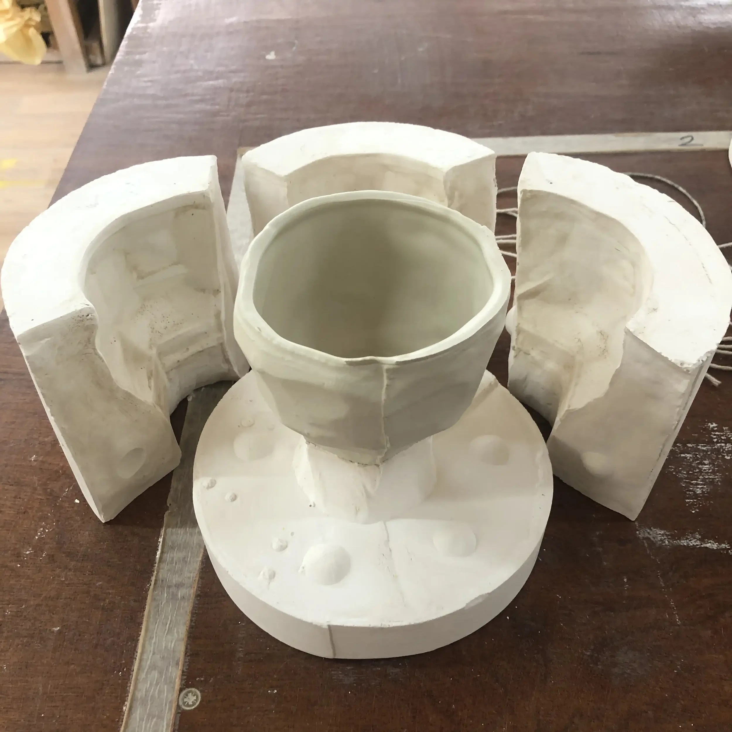 A white plaster mould with a porcelain cup inside placed on a wooden work surface.