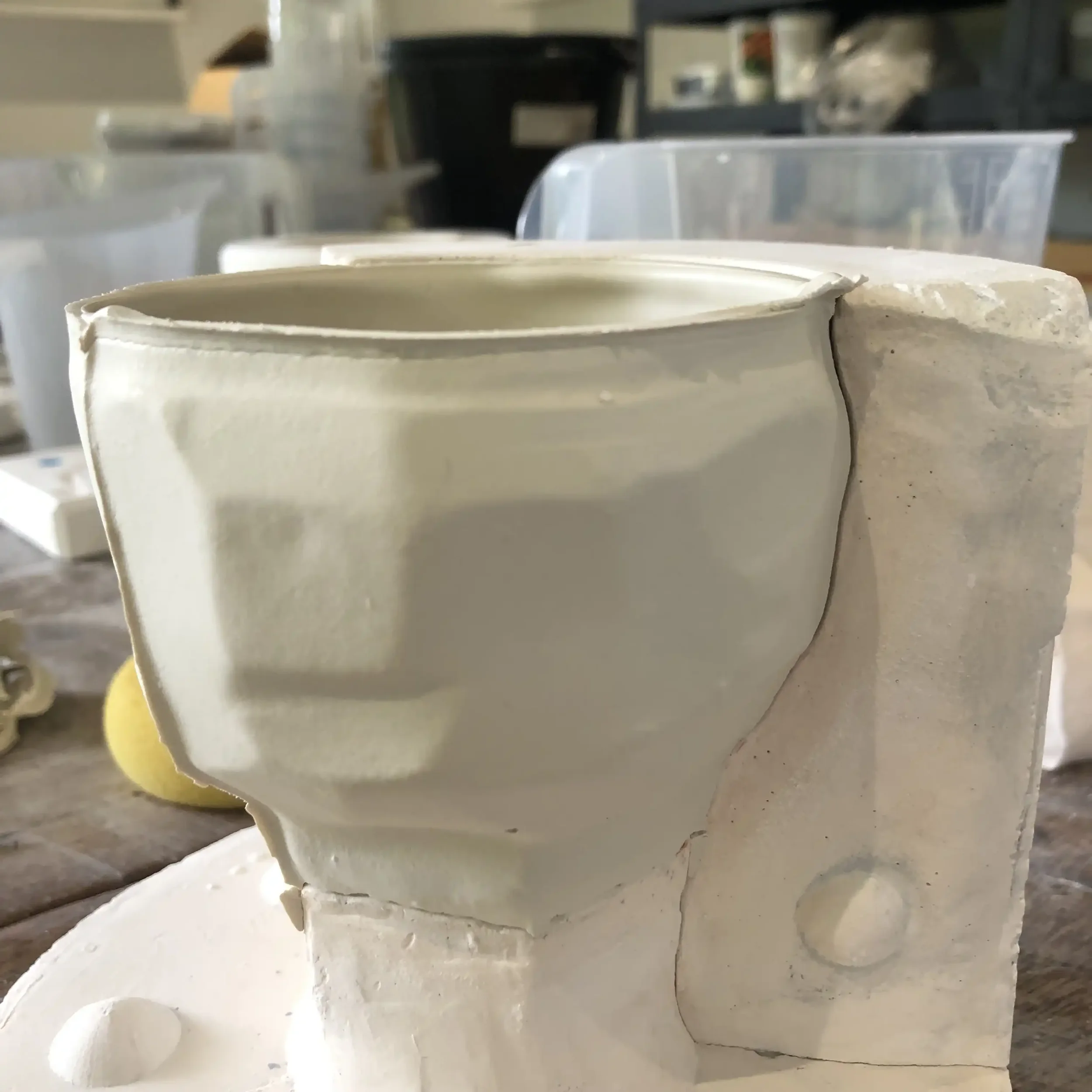 Close-up of a freshly slip-cast porcelain cup on a worktable with the mould that it was made from.