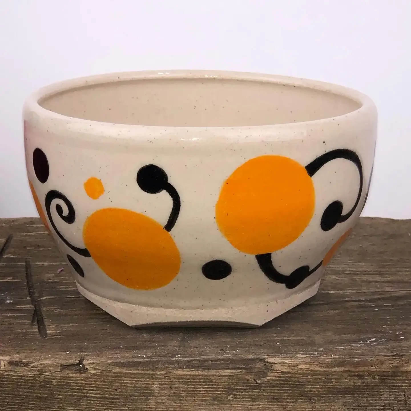 Handmade ceramic bowl with orange and black abstract design, placed on a wooden surface.