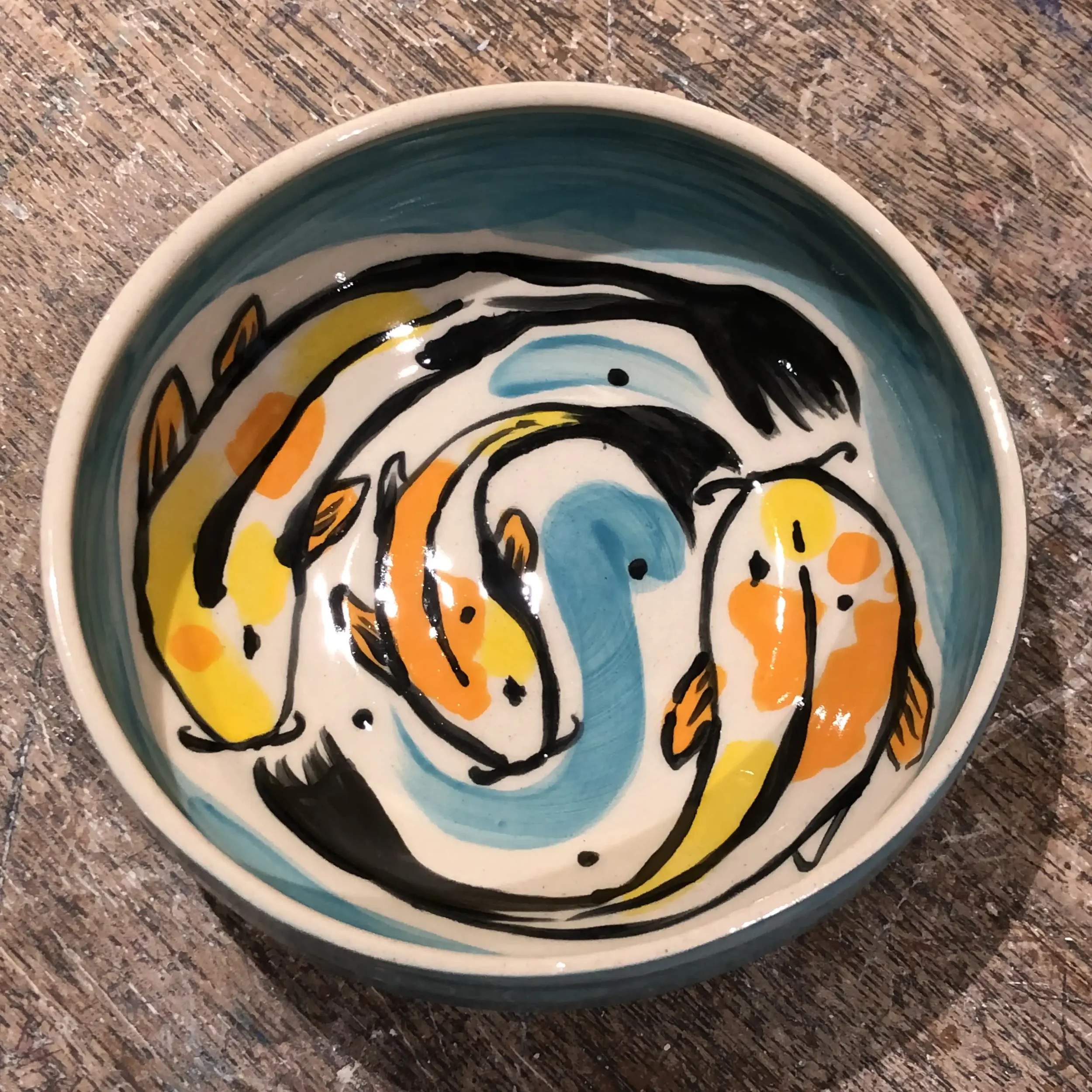 Hand-painted bowl with orange, yellow, black, and blue koi fish swimming in a circular pattern.