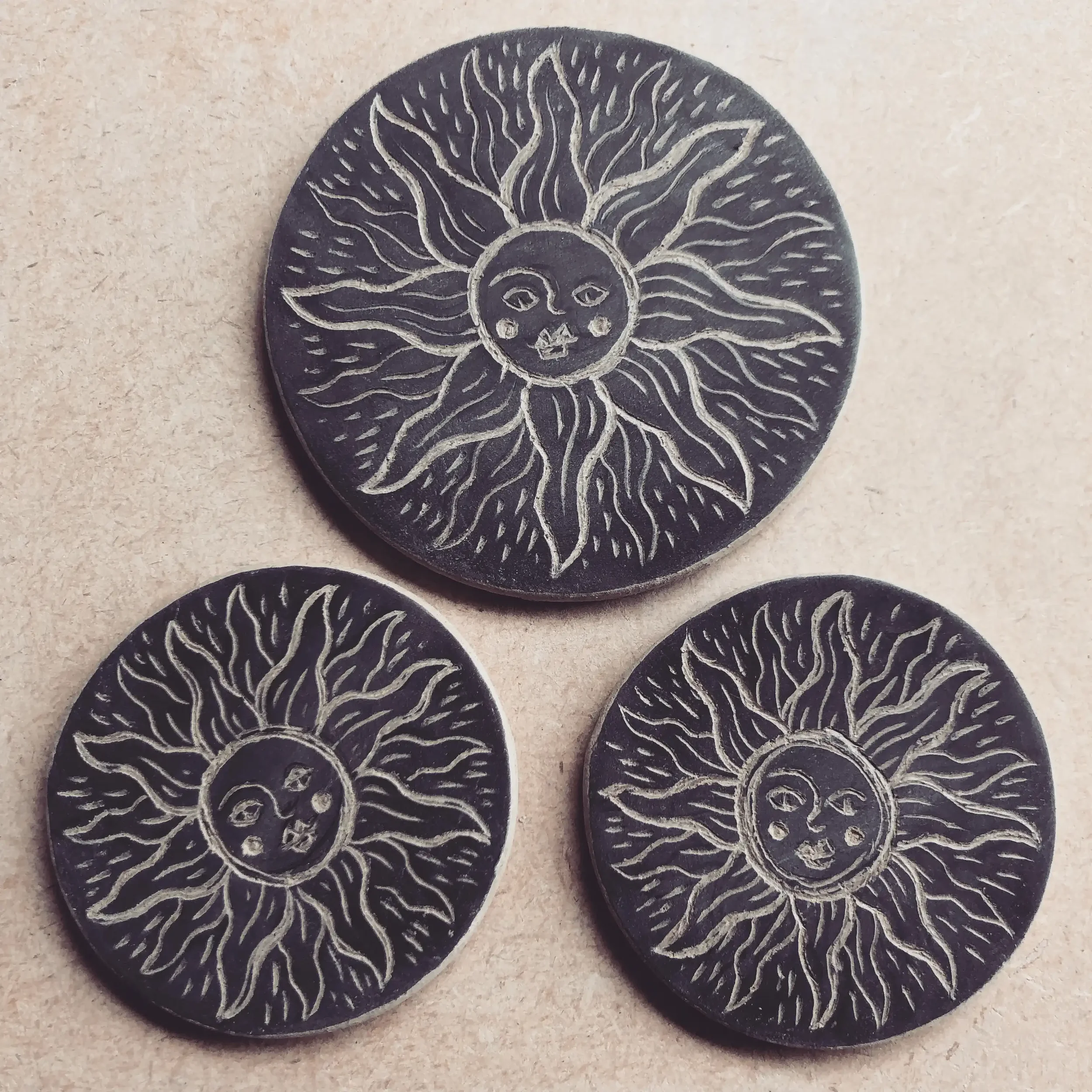 Three black circular tiles with a white sun design featuring a face and wavy rays on a beige background.