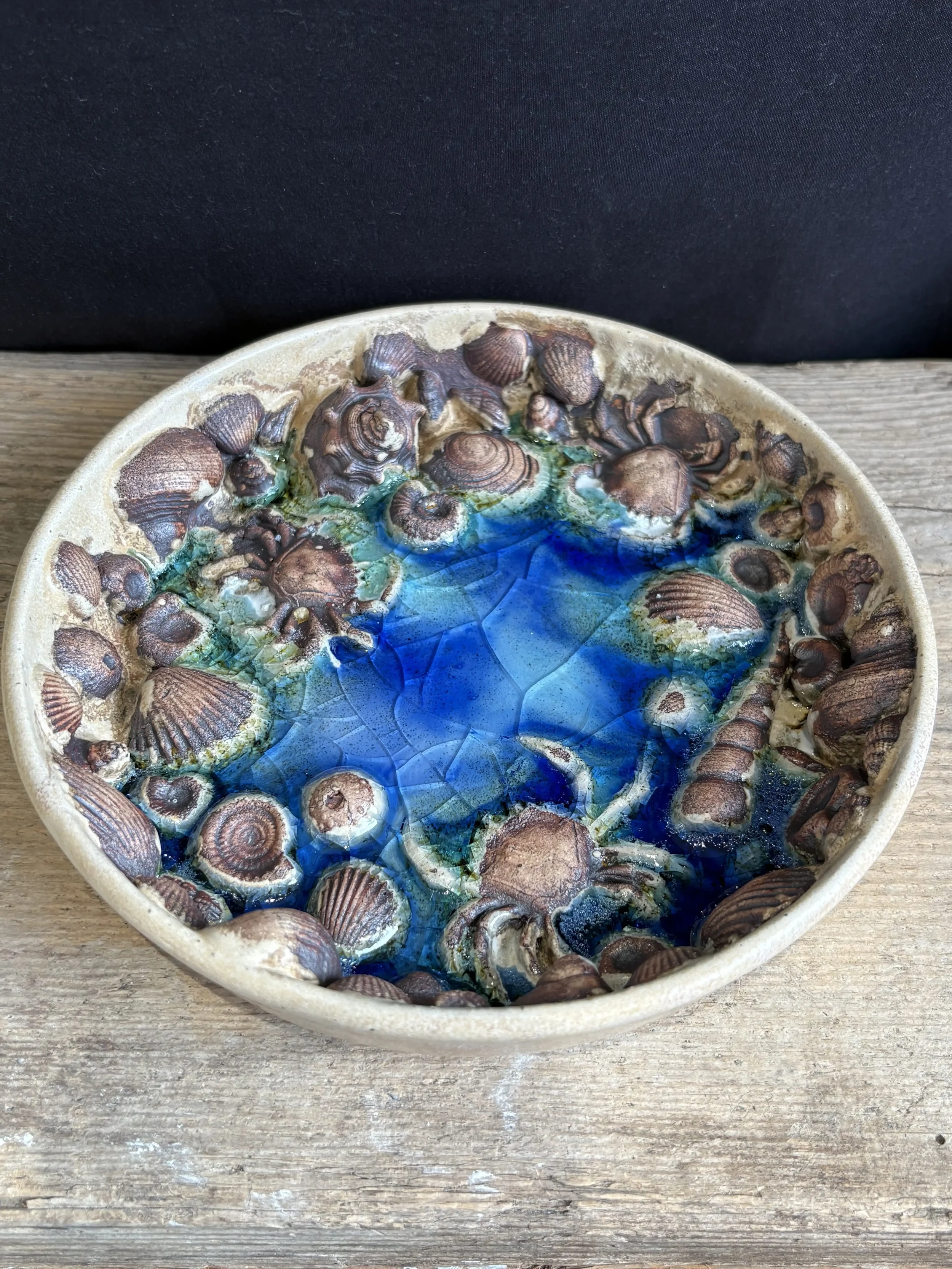 Ceramic bowl with melted blue glass, decorated with seashell and small crabs sitting on a wooden surface.