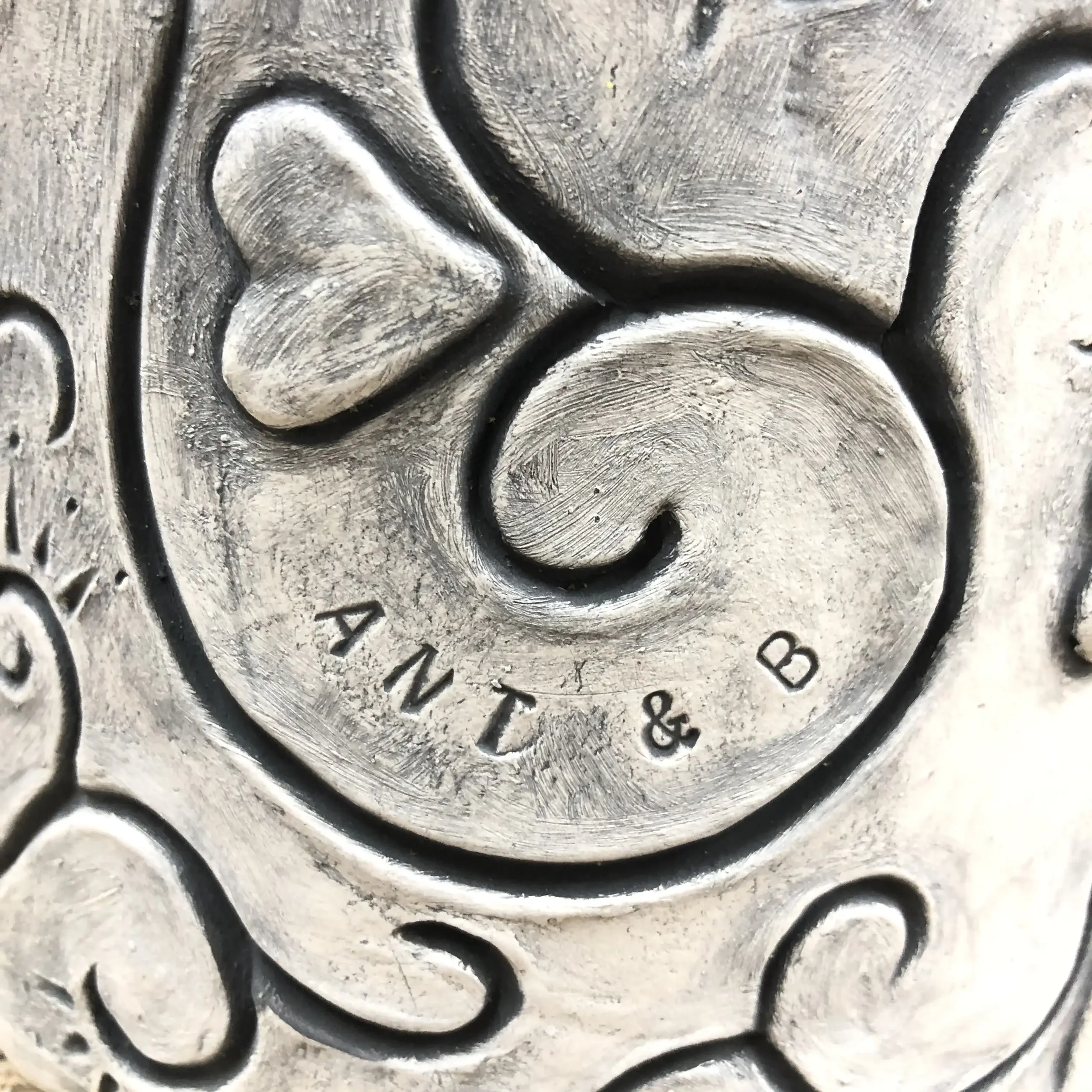 Close-up of a clay pot featuring a heart and swirl design, with the text 'ANT & B' stamped near the centre.