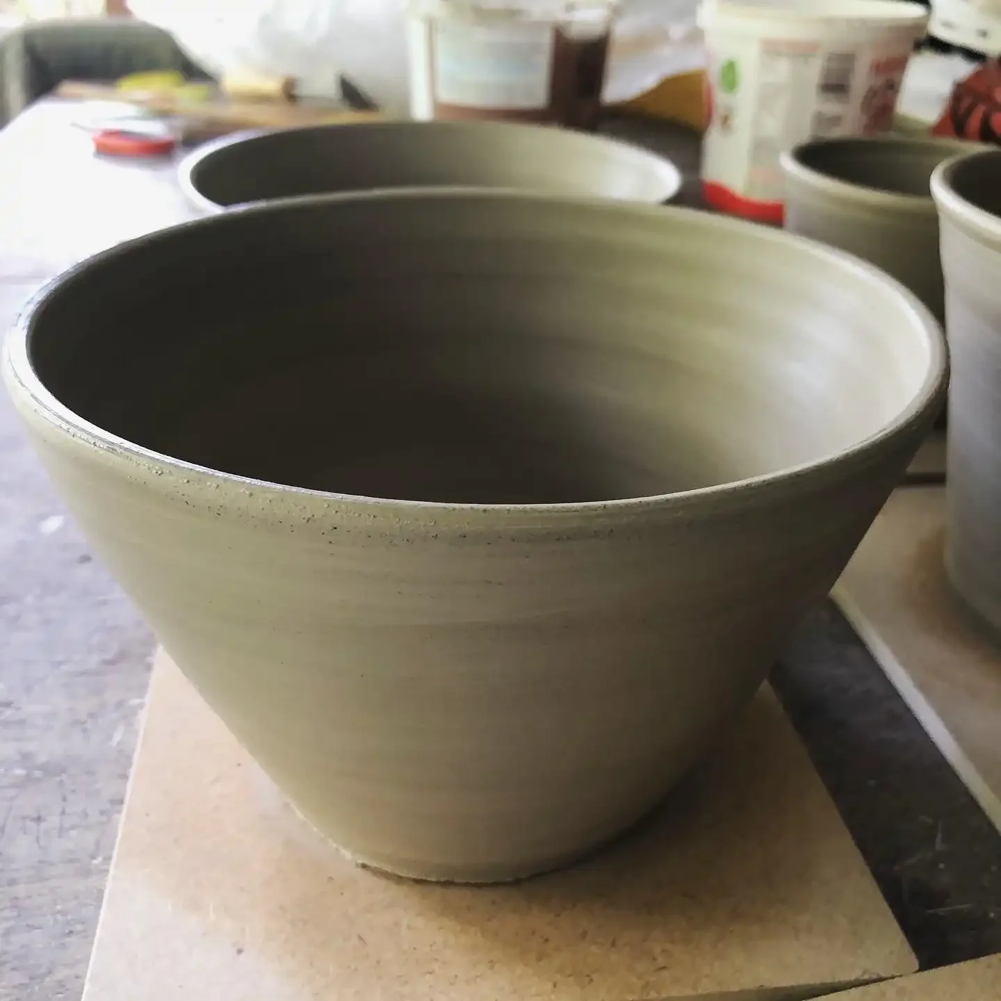 A ceramic bowl in the foreground with additional bowls and pottery supplies in the background, in a pottery studio.