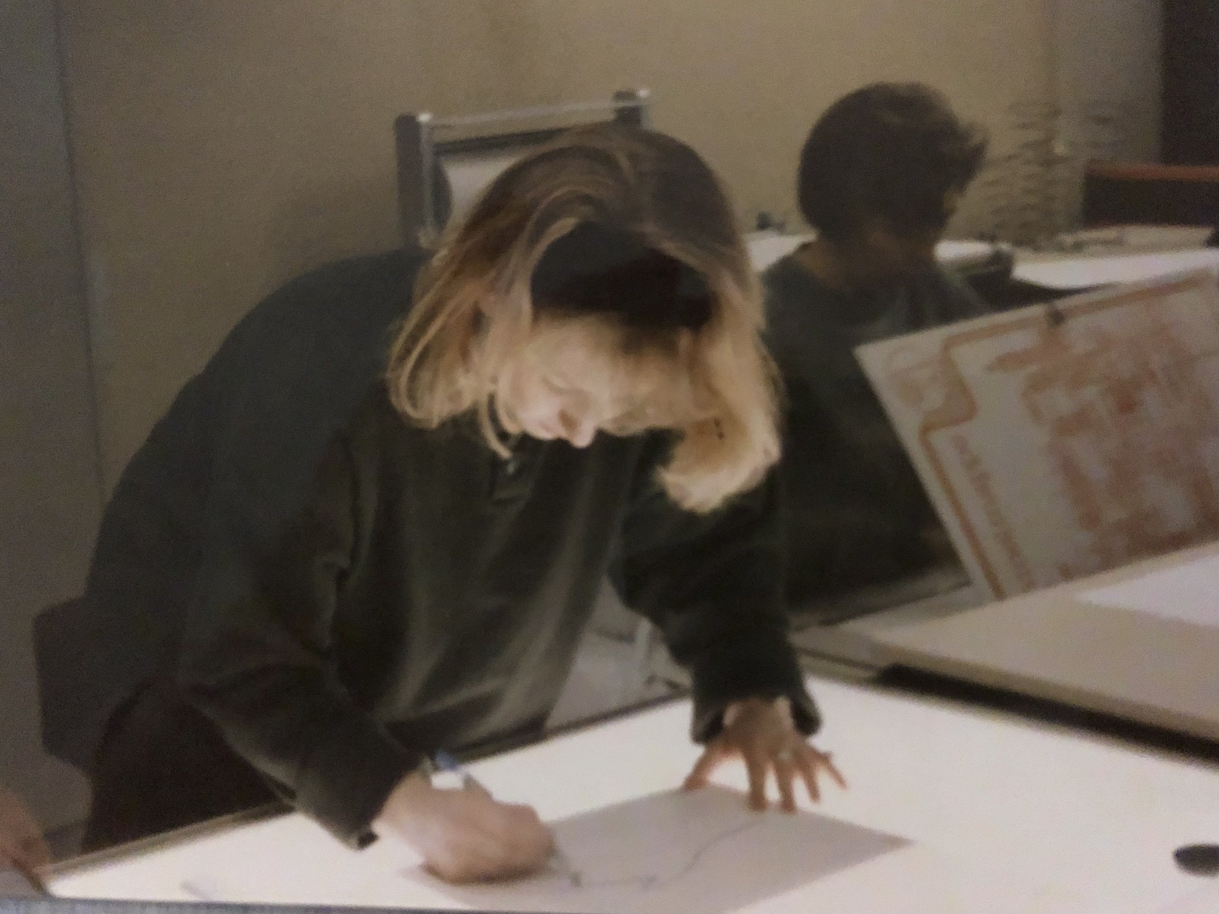 A woman with blonde hair is leaning over a lightbox table, drawing on a piece of paper.