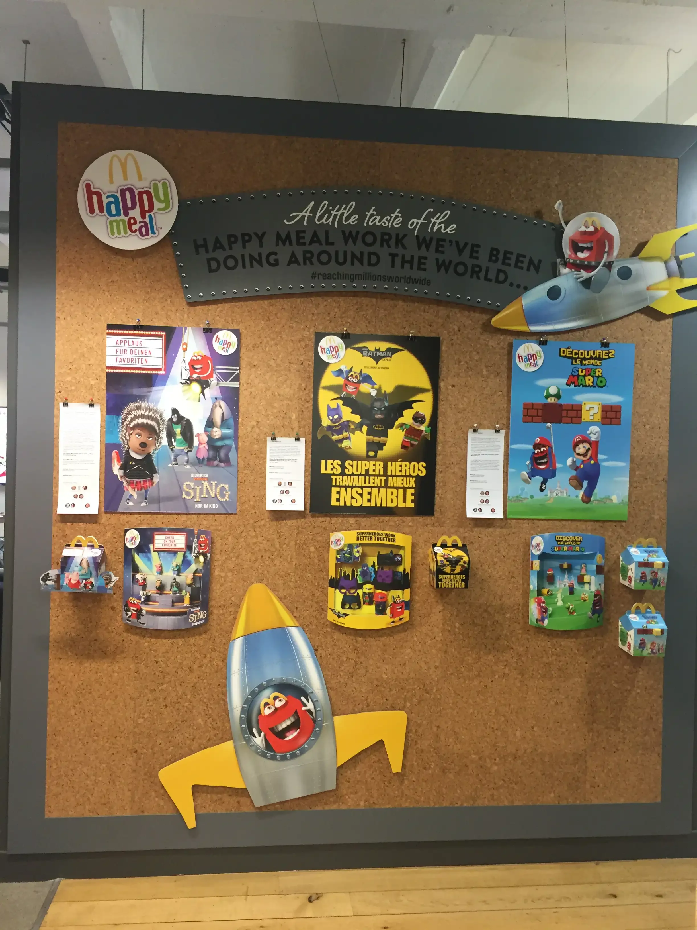 A corkboard display with Marvel superhero and McDonald's Happy Meal themed posters, cutouts, and decorations, including rockets with Happy Meal characters.