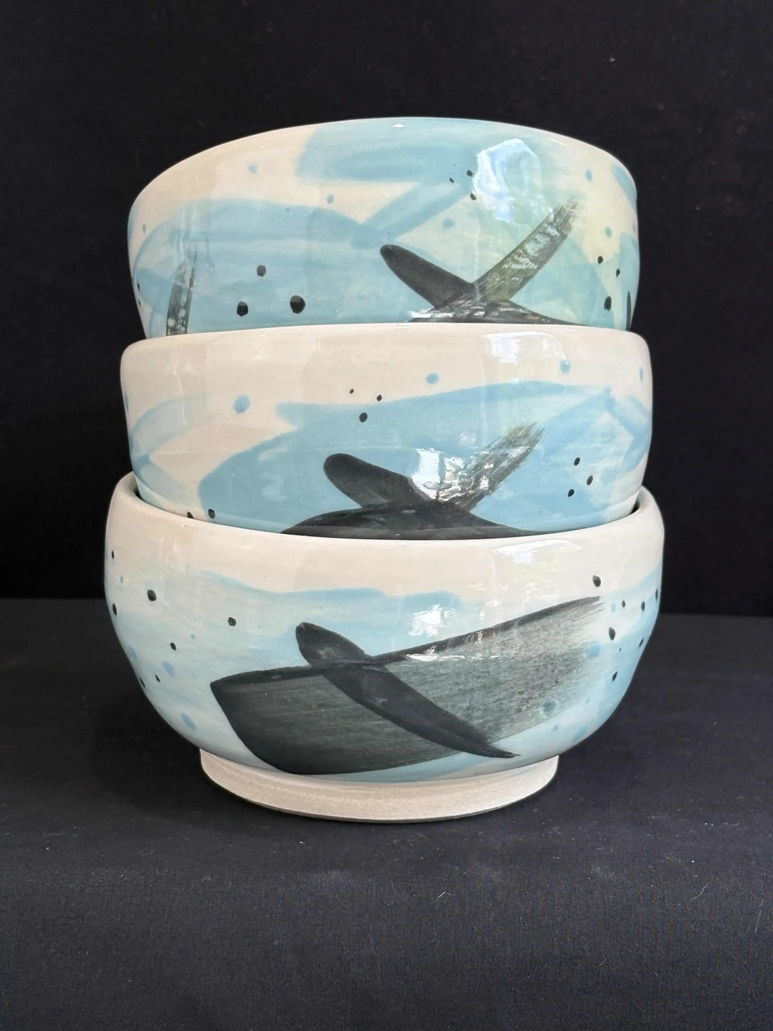 Three stacked ceramic bowls decorated with black and blue brushwork, against a black background.