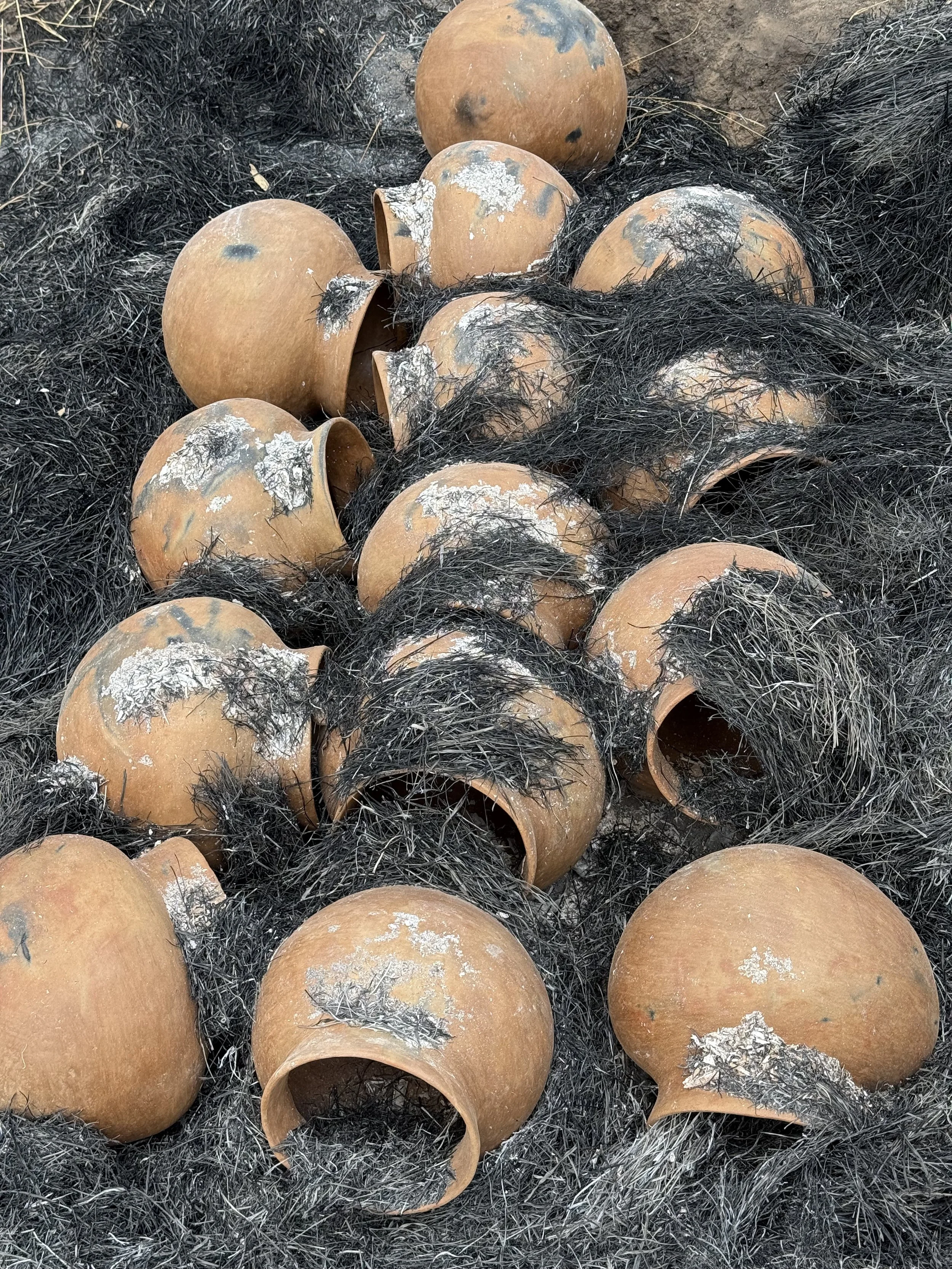 A collection of clay pots and blackened charred material, possibly remnants of a fire, scattered on the ground.