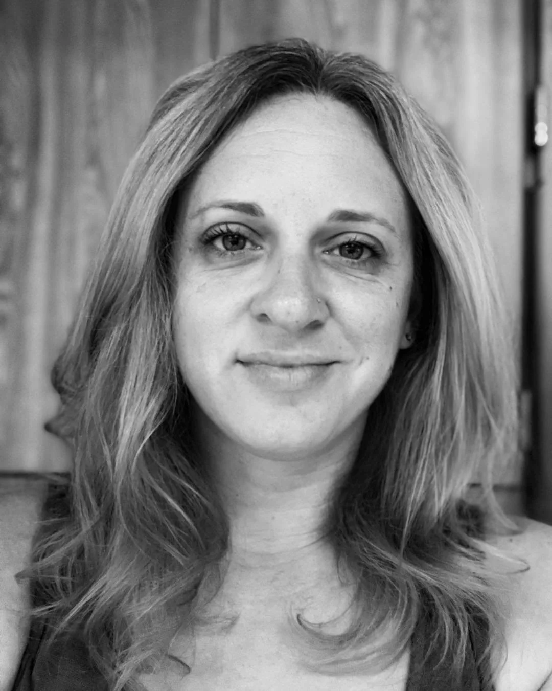 Black and white portrait of a woman with wavy hair, smiling softly, in front of a wooden background.