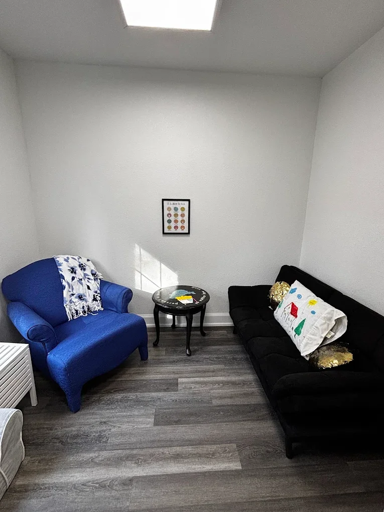 Living room with a blue armchair, black sofa with pillows, round side table, and framed poster on the wall