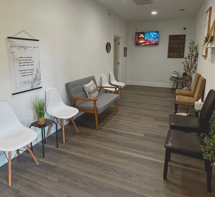 Empty waiting room with modern chairs, a gray sofa, potted plant, wall art, and a TV