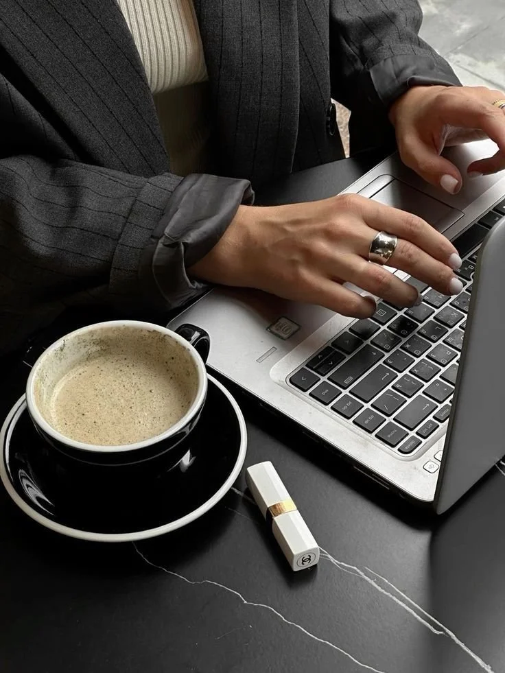 Person wearing a suit typing on a laptop with a cup of coffee and a USB flash drive on the black desk.
