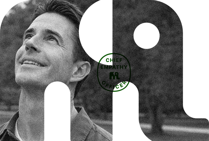 Black and white portrait of a smiling man looking upward, outdoors, with a park and trees in the background.