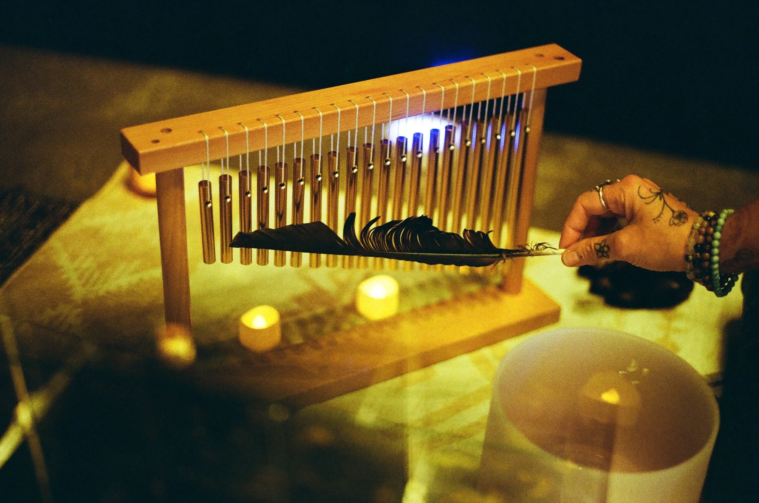 Person holding a feather near a wooden chime instrument with candles in the background.