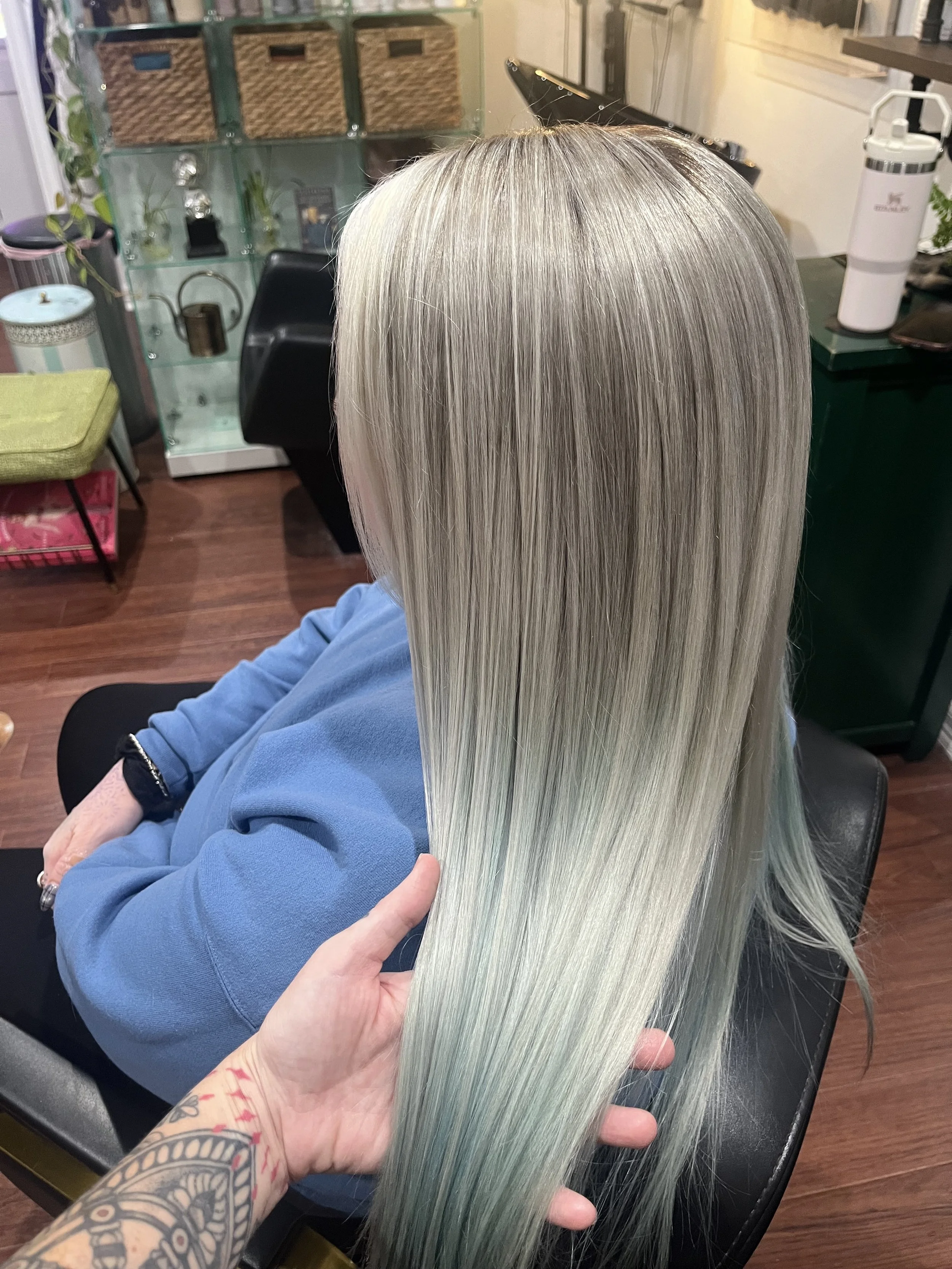 Person with straight, long, platinum blonde hair sitting in a salon chair, with a hand gently holding a section of their hair.
