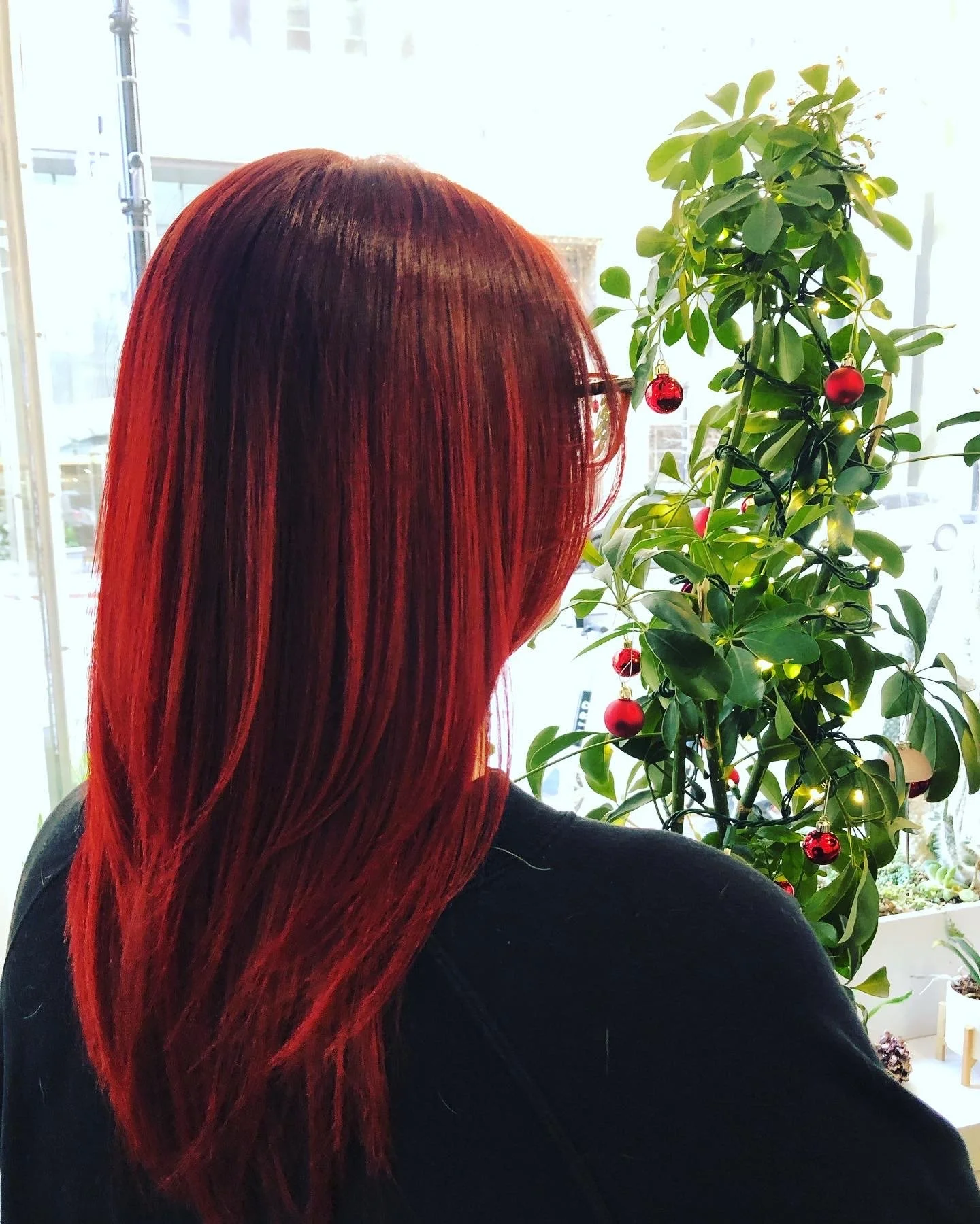 Person with long, straight red hair standing near a decorated Christmas tree indoors.