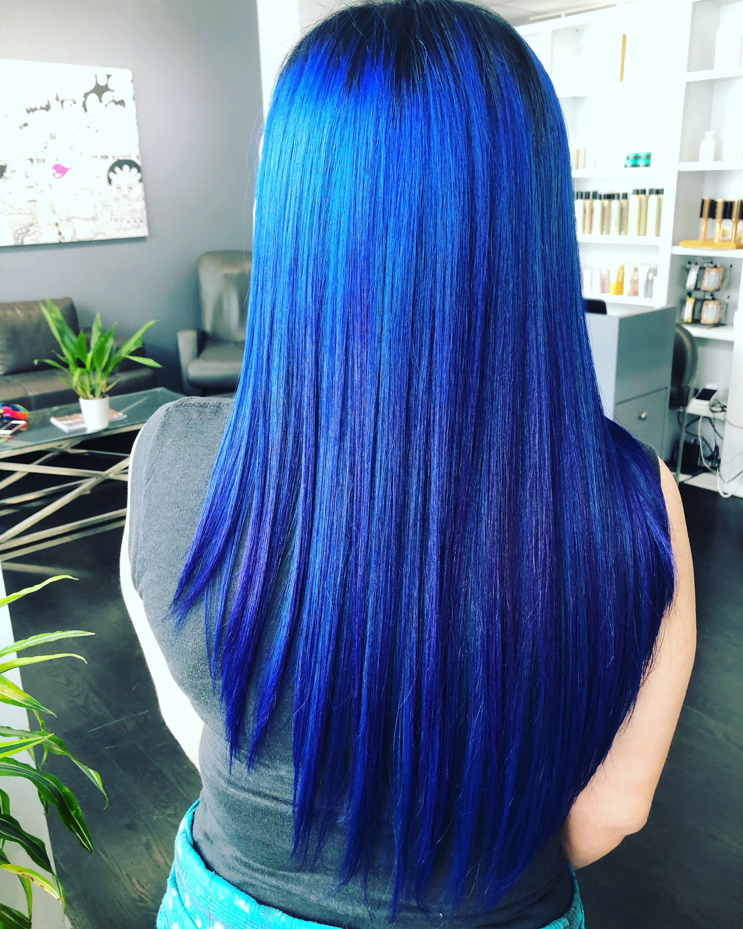 Person with long, straight, vibrant blue hair in a salon.