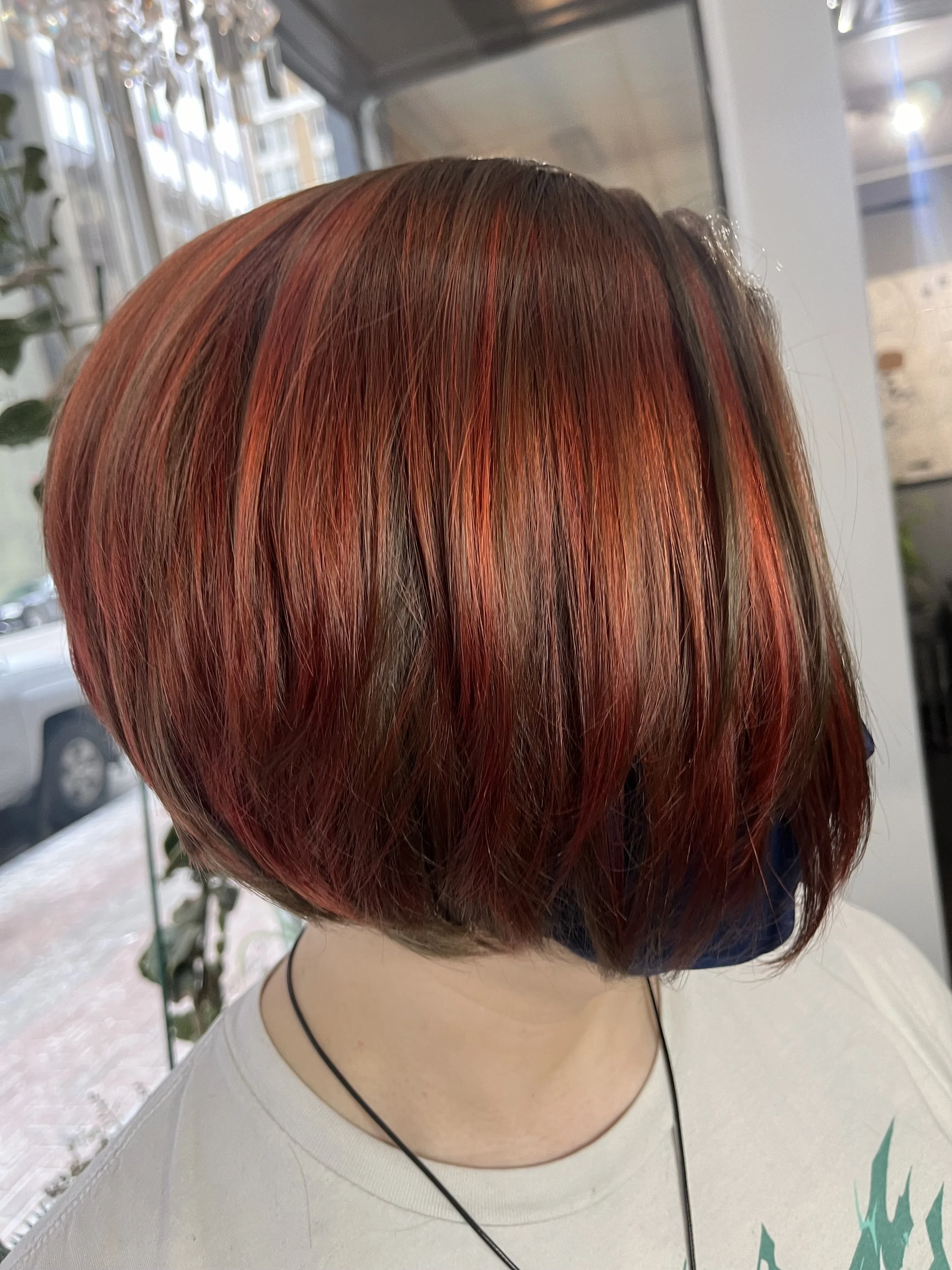 A person with short, layered hair dyed in shades of red, orange, and brown, seen from behind.