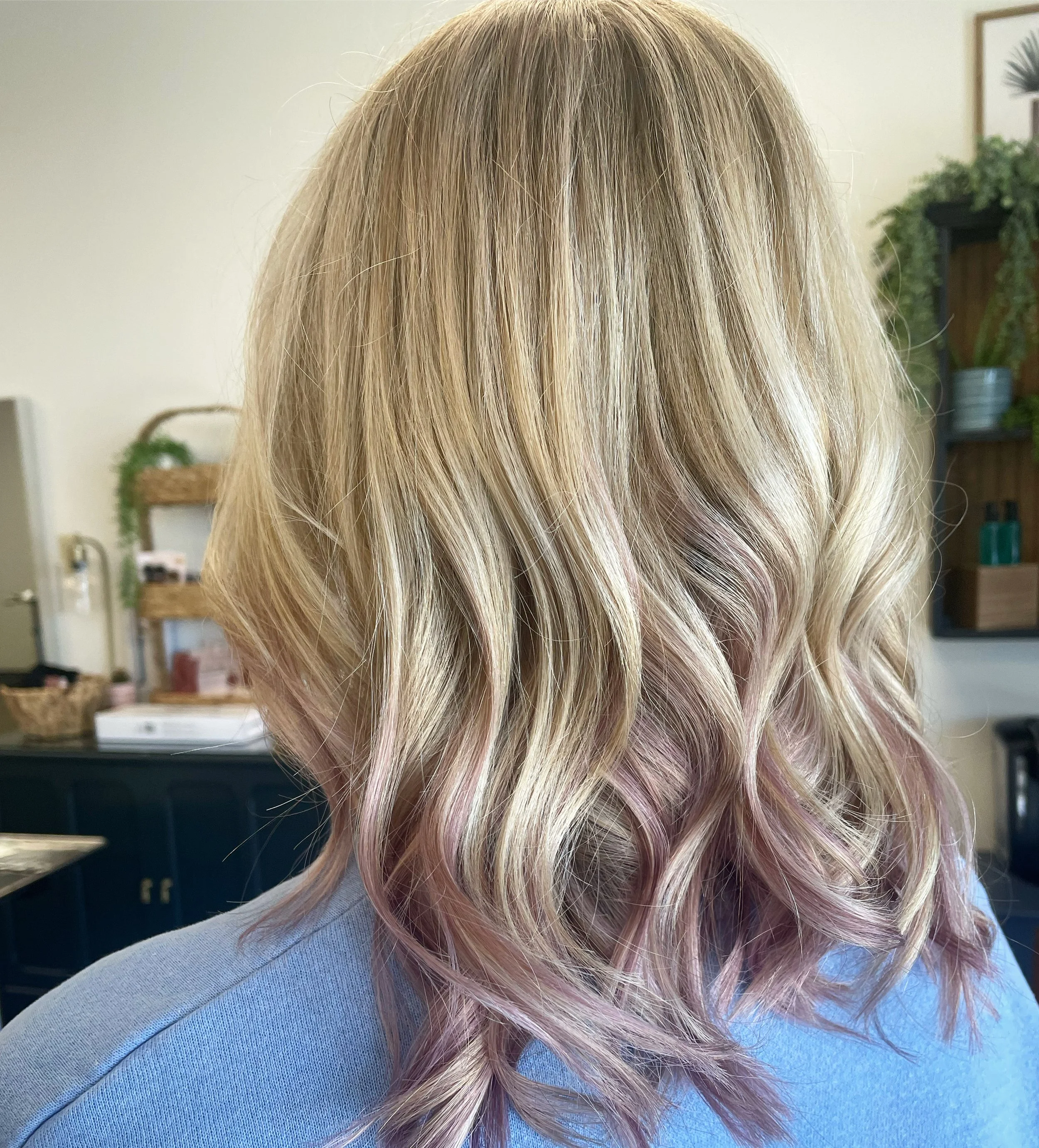 Back view of shoulder-length blonde hair with soft pink highlights styled in loose waves.