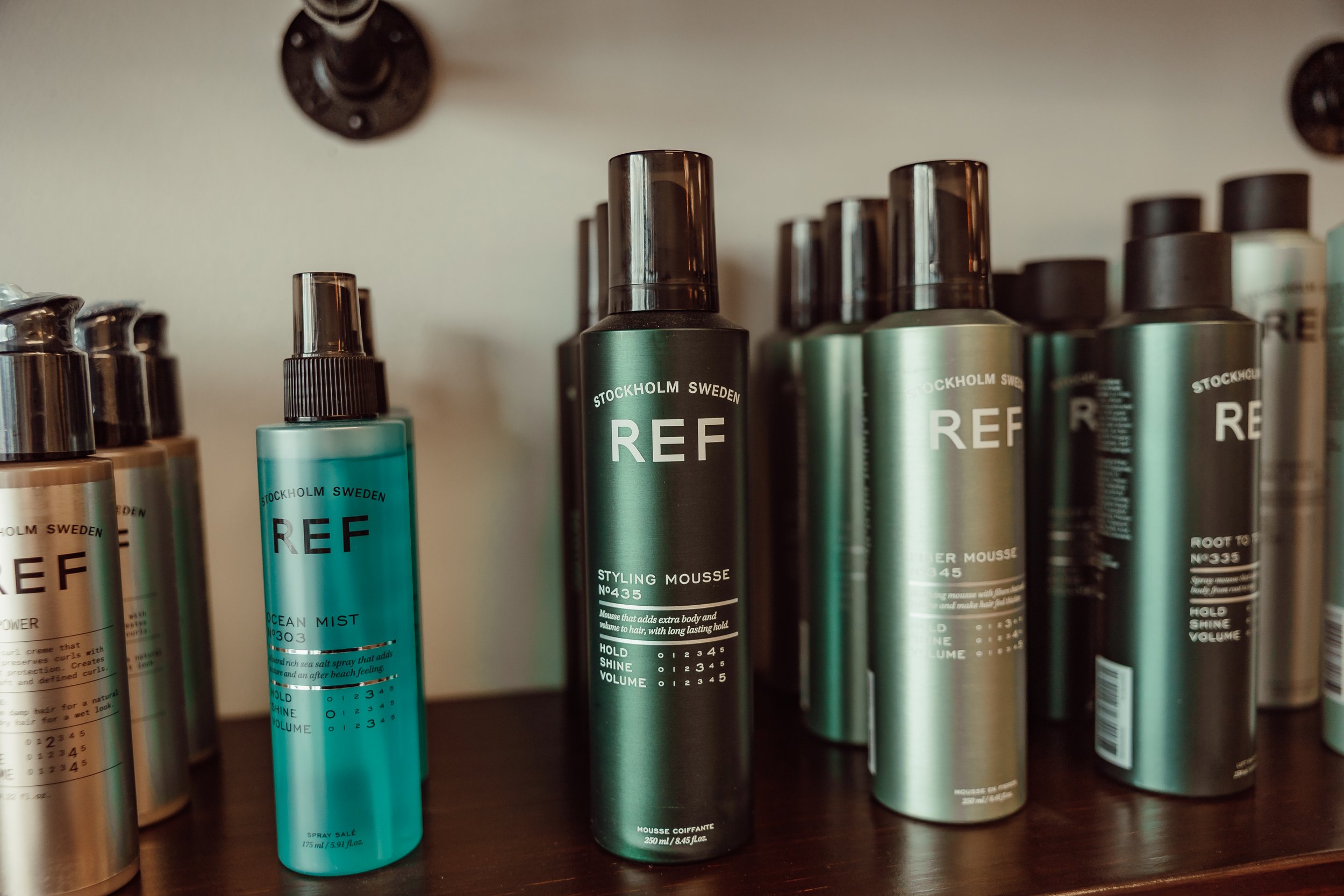 Collection of REF hair styling products on a wooden surface, including styling mousse and ocean mist spray bottles.
