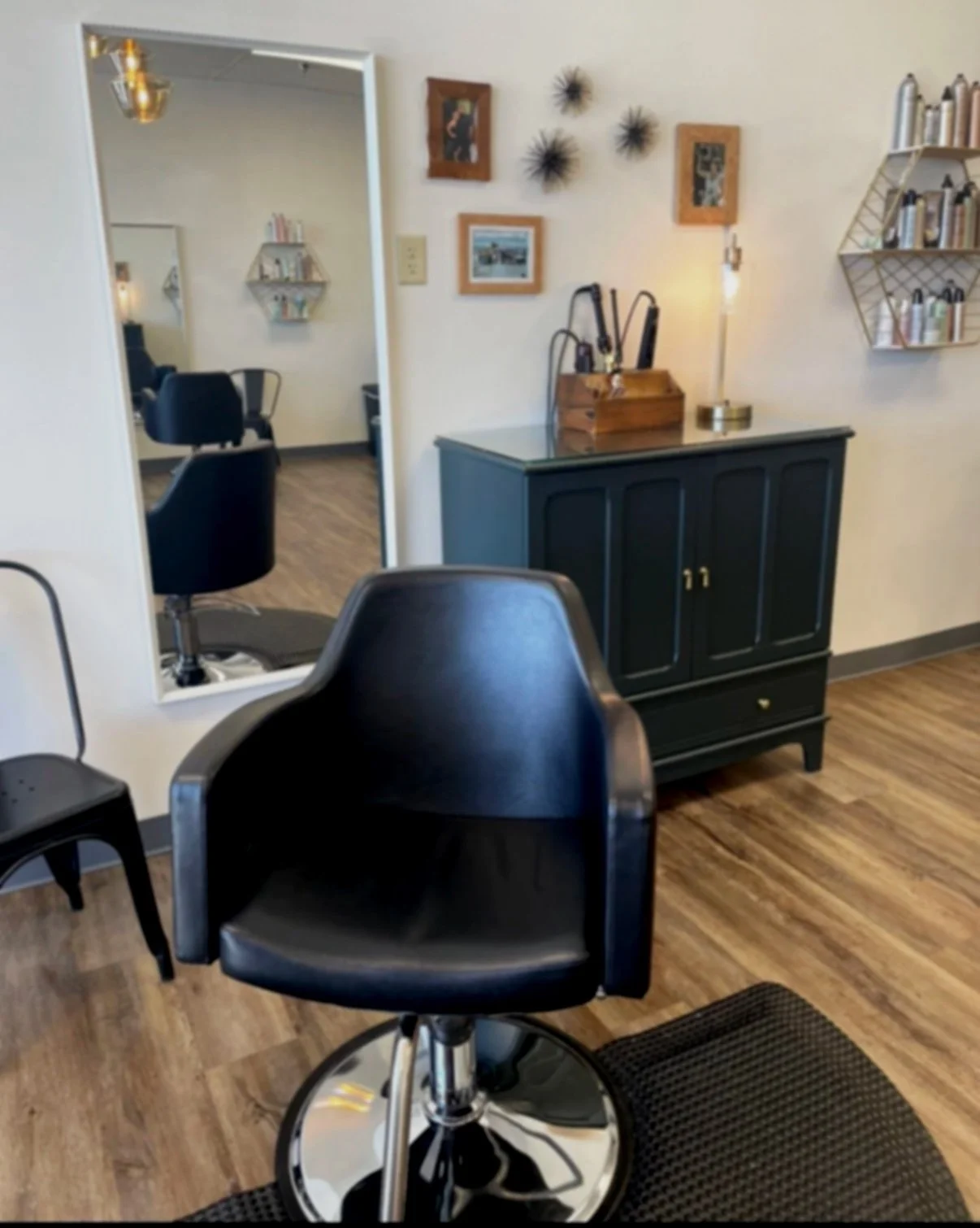Interior of a hair salon with styling chairs, mirrors, wooden flooring, and a sideboard with decor and hair products.