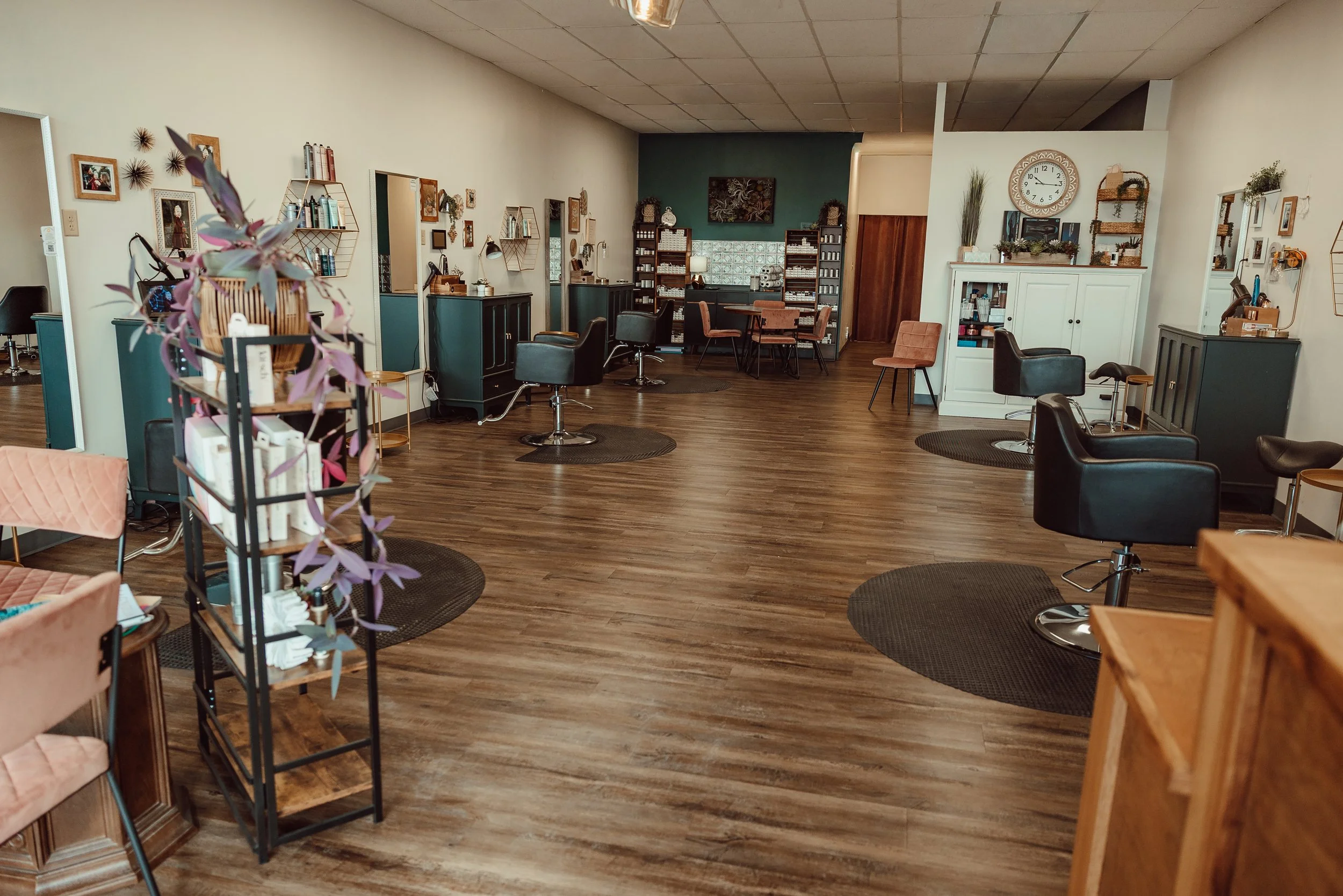 Interior of a hair salon with multiple styling stations, black salon chairs, wooden floors, and decorative wall decor.