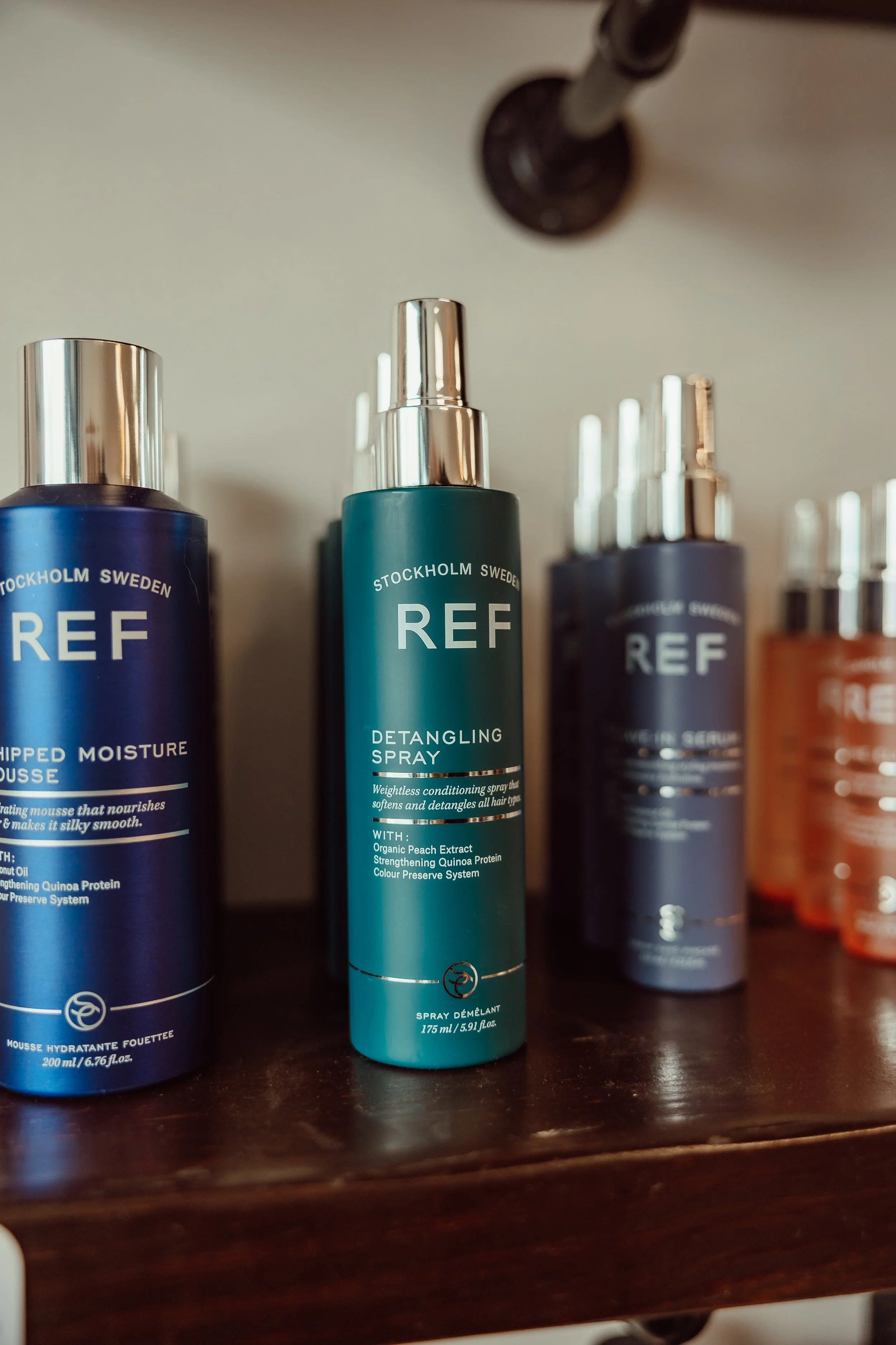REF detangling spray bottle on a wooden shelf with other REF hair care products.