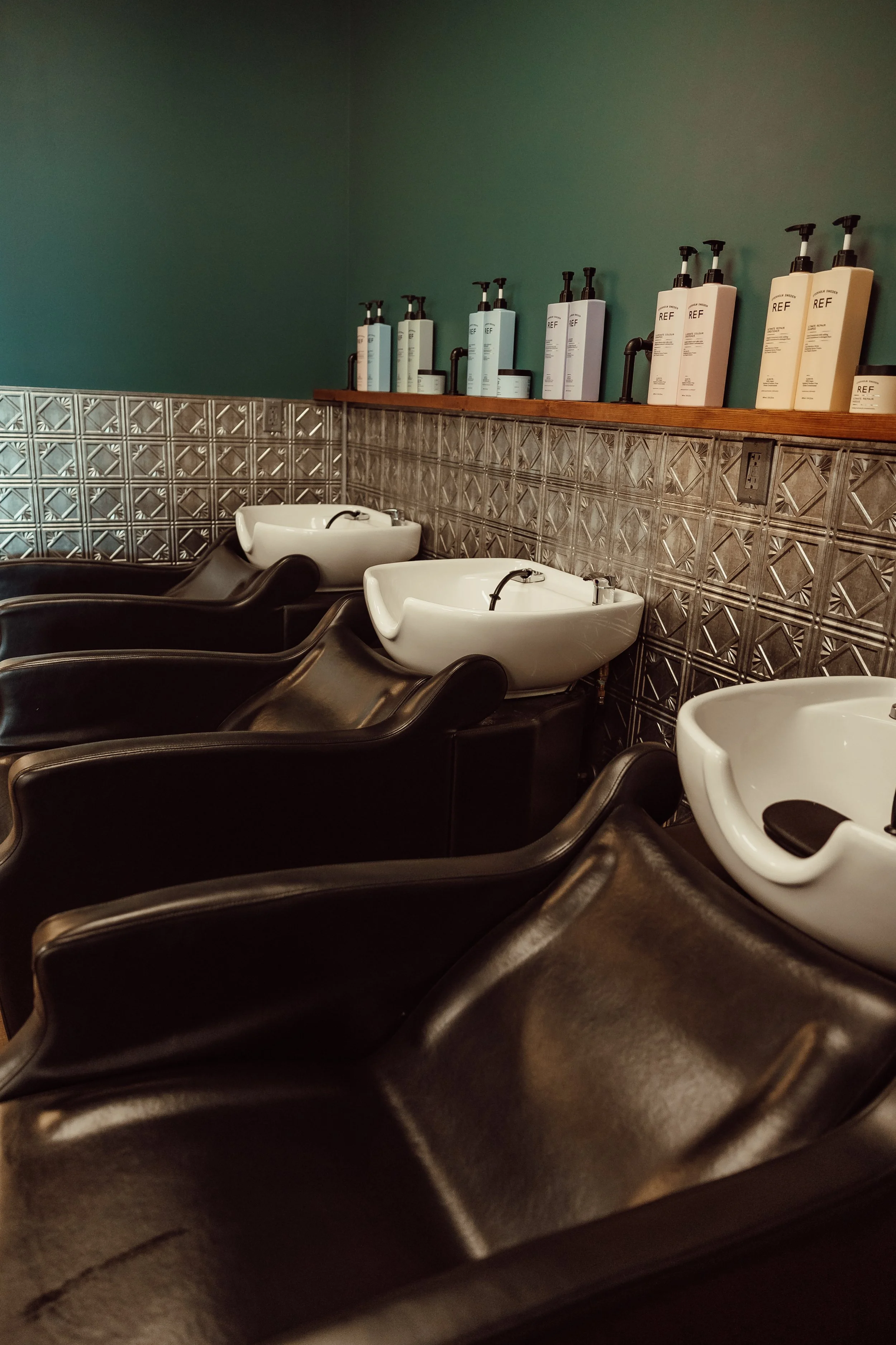 Hair wash sinks in a salon with black chairs and shelves of hair care products.