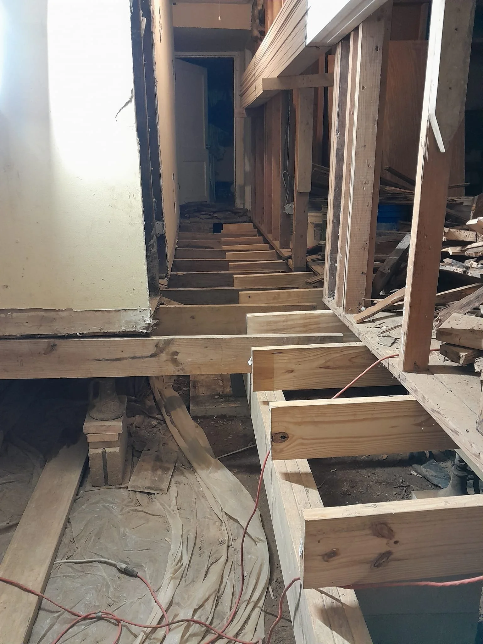 Construction site with wooden framing for a floor, exposed beams, and construction materials. A doorway is visible in the background.