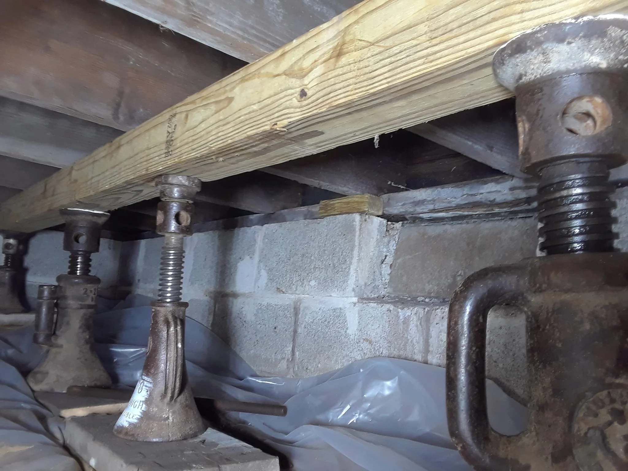 Jacks supporting a wooden beam to a brick wall in a construction or repair setting.