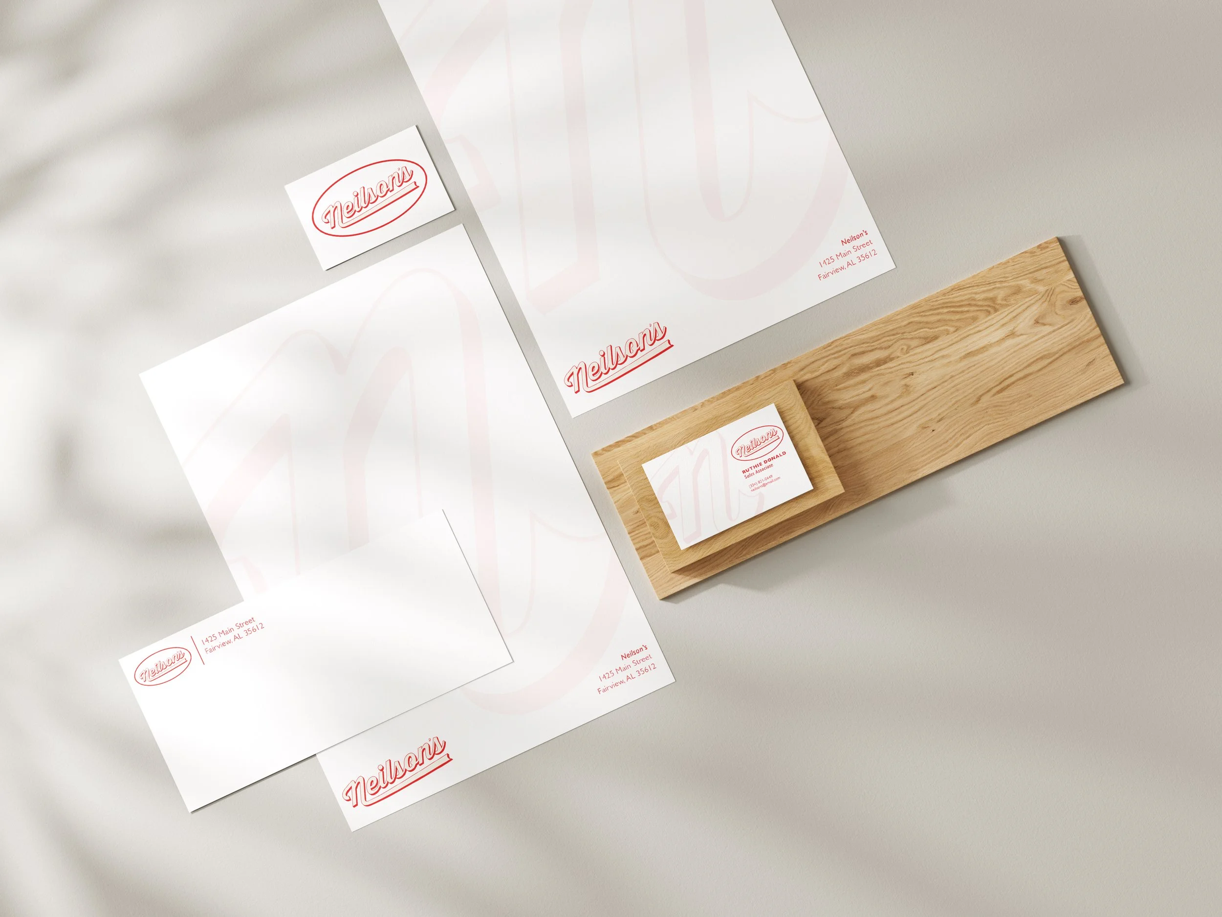 Set of branded stationery items including business cards, envelopes, and letterhead with red Neilson's logo, arranged on a white surface with a wooden stand.