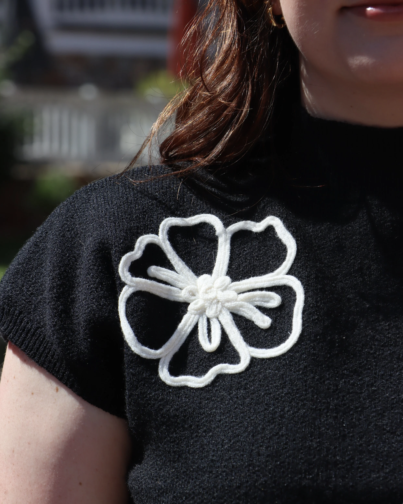 Close-up of a woman's black top with a white embroidered flower patch on the shoulder.