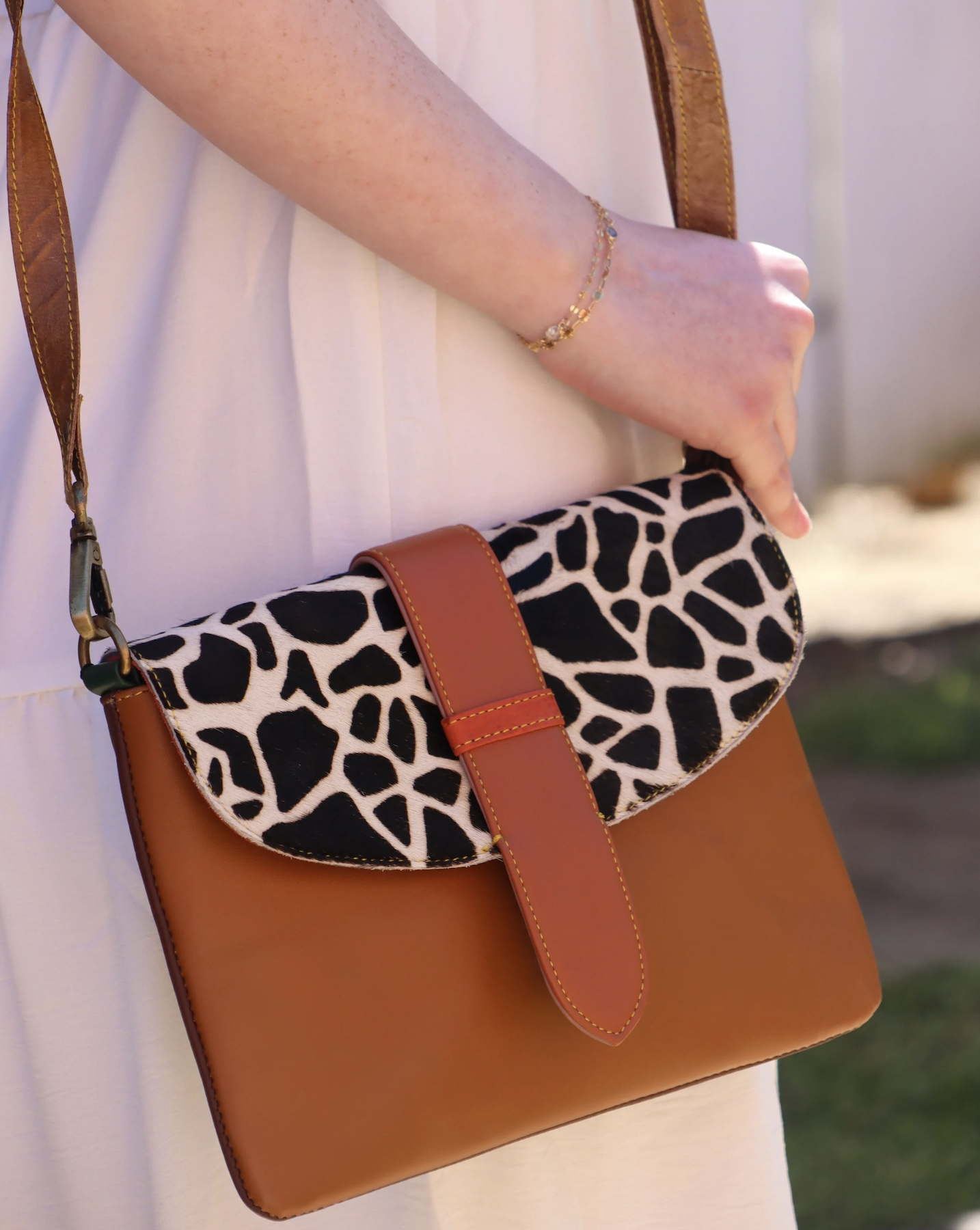 Close-up of a woman's hand with a gold bracelet, holding a stylish brown and animal print handbag.