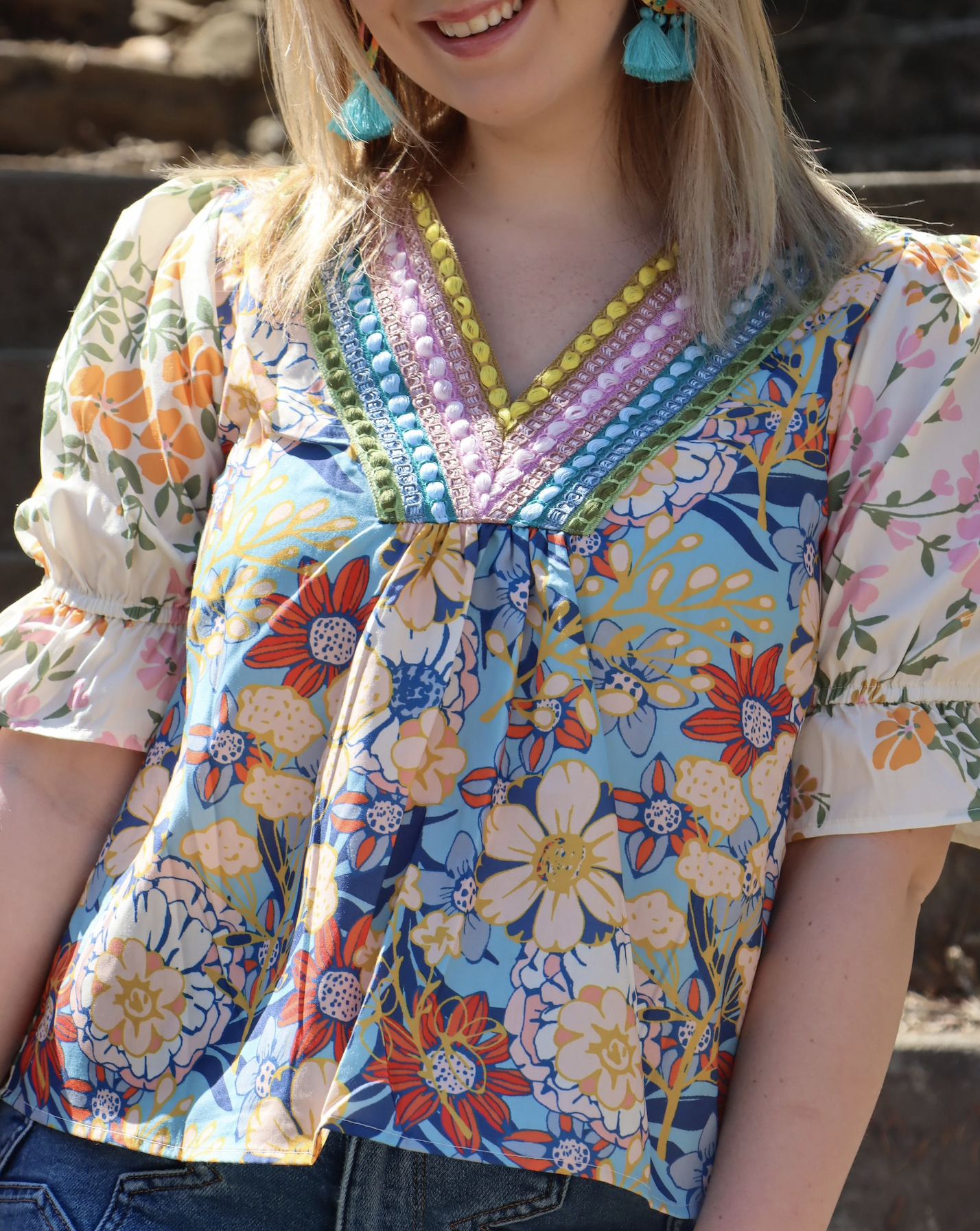 Close-up of a woman wearing a colorful floral blouse with embroidered neckline and tassel earrings.