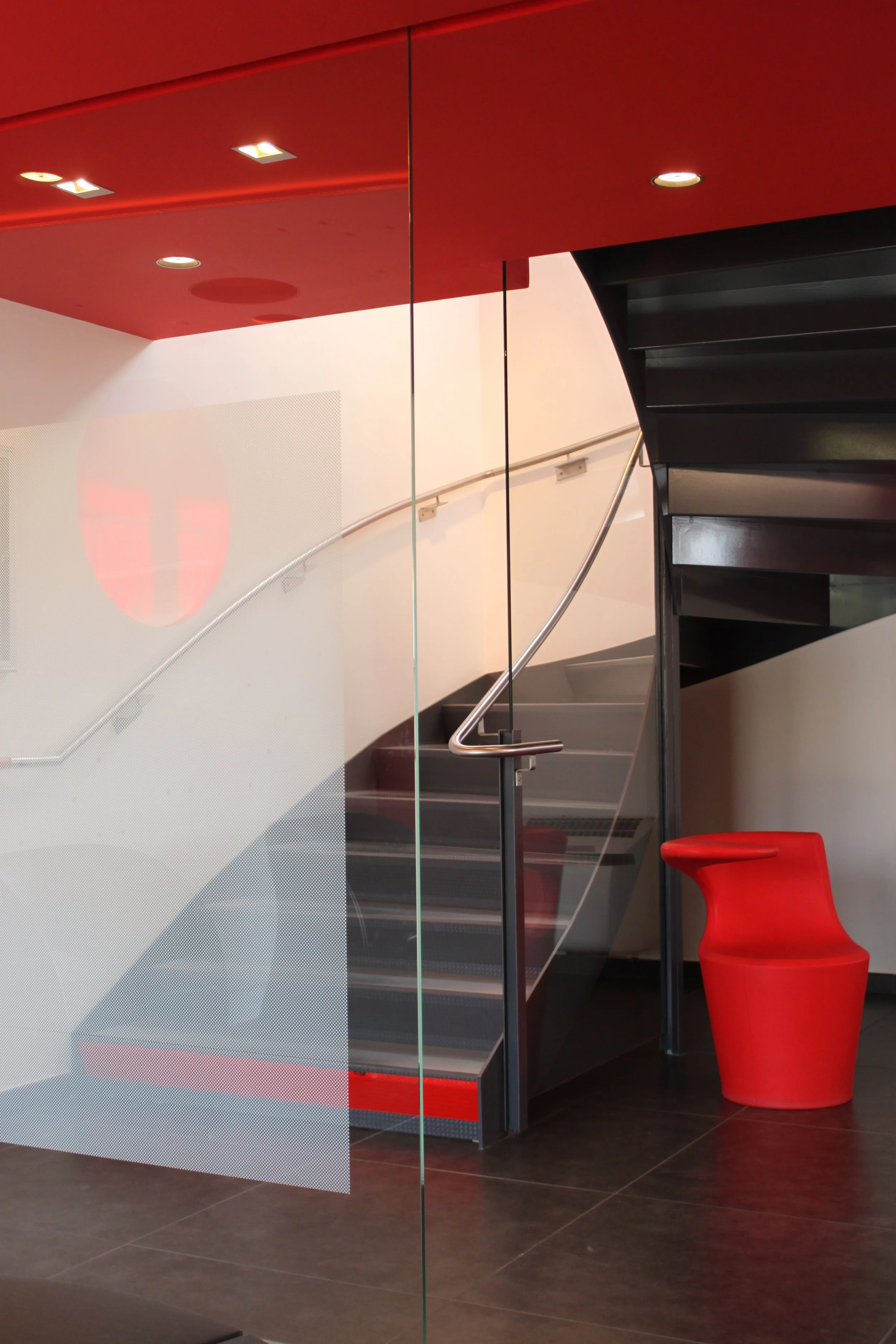 Escalier en métal noir avec rampe en acier inoxydable et chaise rouge dans le coin d'une pièce moderne avec plafond rouge et mur blanc