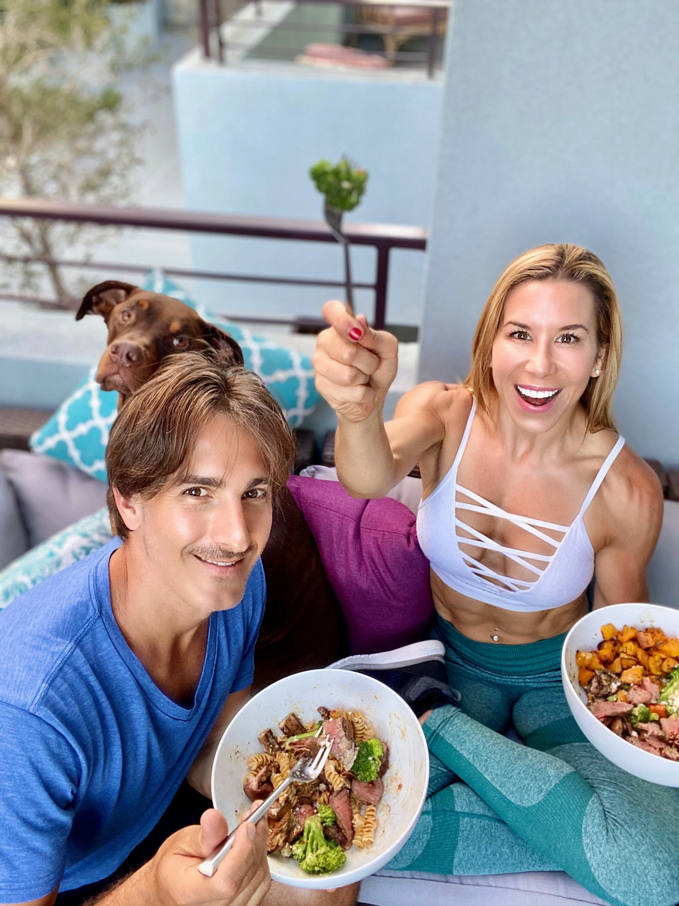 A fit woman with toned muscles posing with hands on hips, wearing a blue sports bra and black leggings against a gray background.