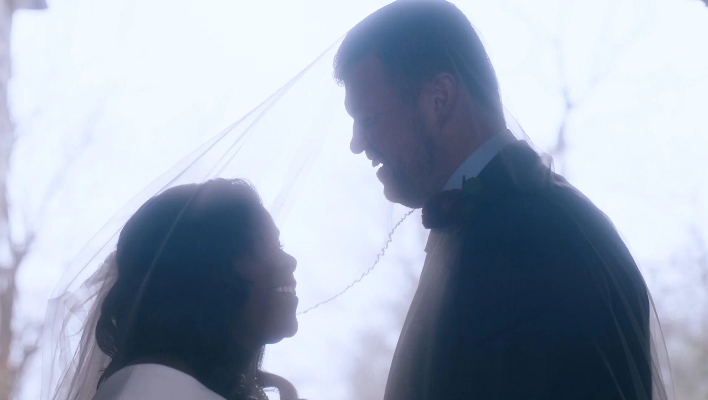 A bride and groom standing close together under a veil, smiling at each other during their wedding.
